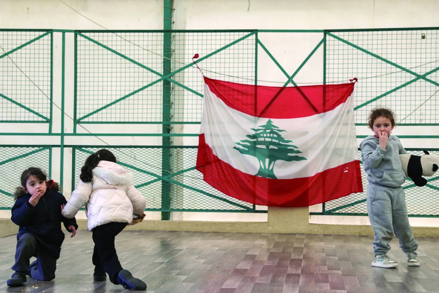 أطفال نازحون يلعبون في مدرسة تحولت إلى مركز للنزوح ومن خلفهم العلم اللبناني (رويترز)