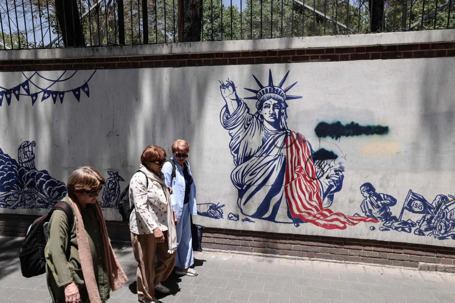 Iranian women walk past anti-US murals outside the former US embassy in Tehran on June 15, 2026. (AFP)