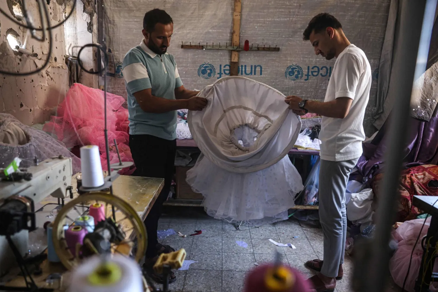 Palestinian dressmakers add skirt hoops to a child's gown, at a workshop where dresses are created including evening and wedding gowns despite limited resources and old dresses are recycled, in the city of Khan Yunis in the southern Gaza Strip on June 13, 2026. (Photo by BASHAR TALEB / AFP) / 