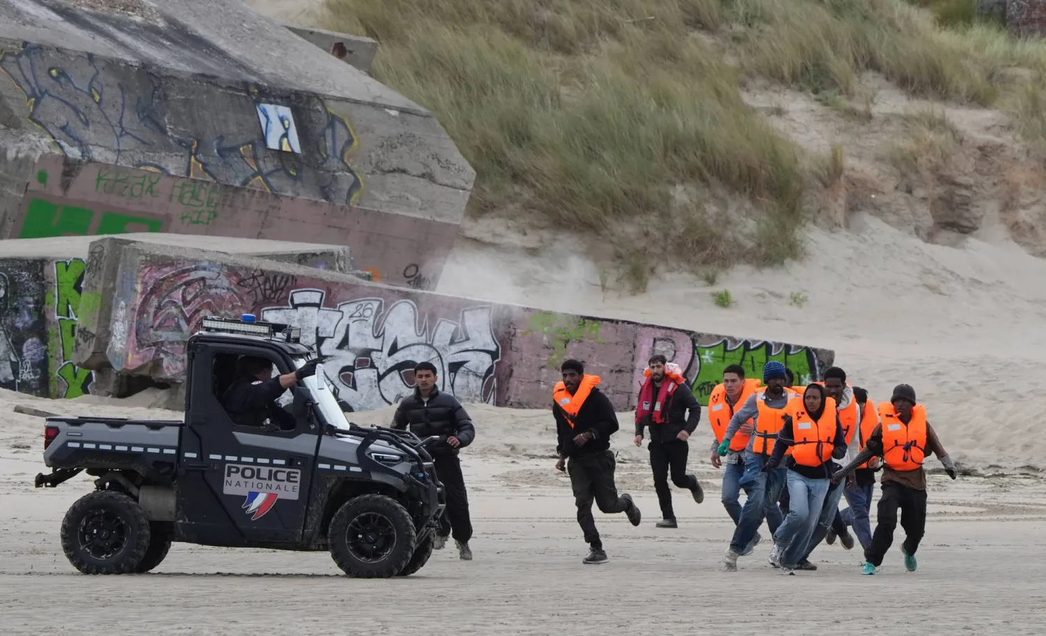 15 June 2026, France, Berck: People thought to be migrants, who were previously detained by the French police, run across the sand as they try to board a small boat off the coast of Berck, France, during an attempt to cross the English Channel. Photo: Gareth Fuller/PA Wire/dpa