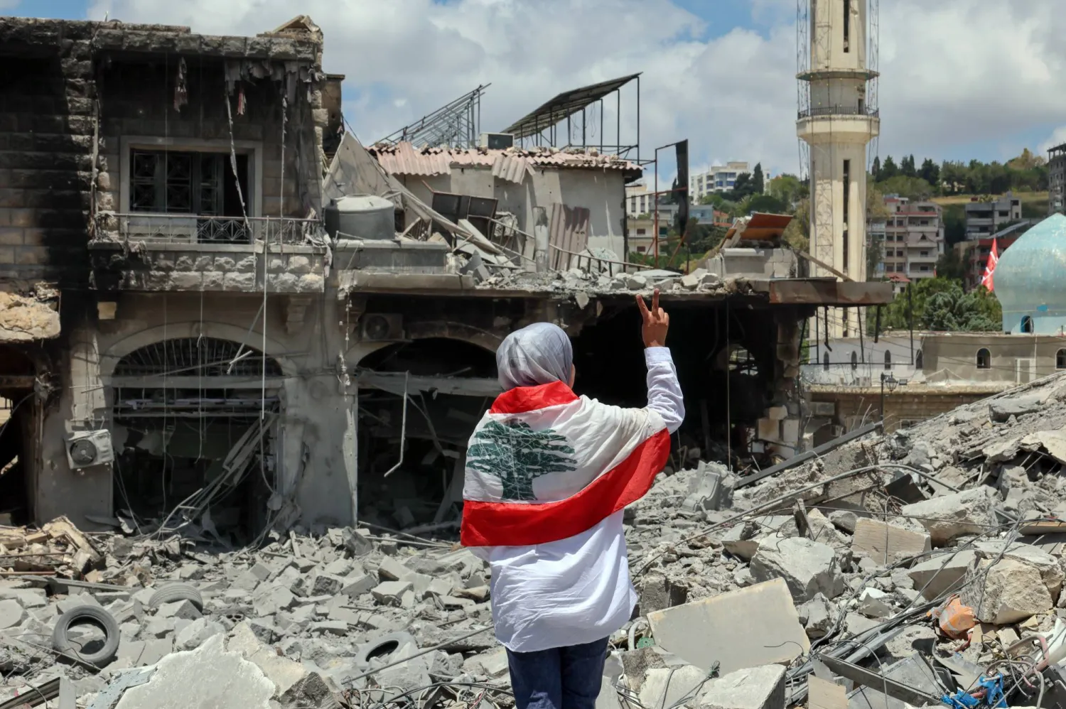 لبنانية تضع العَلَم اللبناني على كتفيها وتتفقد الدمار في ساحة مدينة النبطية بجنوب لبنان (إ.ب.أ)