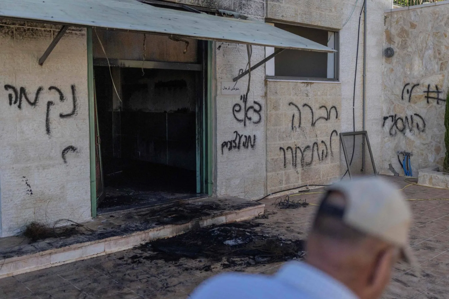 فلسطيني يمر بجانب مسجد متضرر بعدما أضرم مستوطنون إسرائيليون فيه النار في جلجليا بالضفة الغربية (أ.ف.ب)