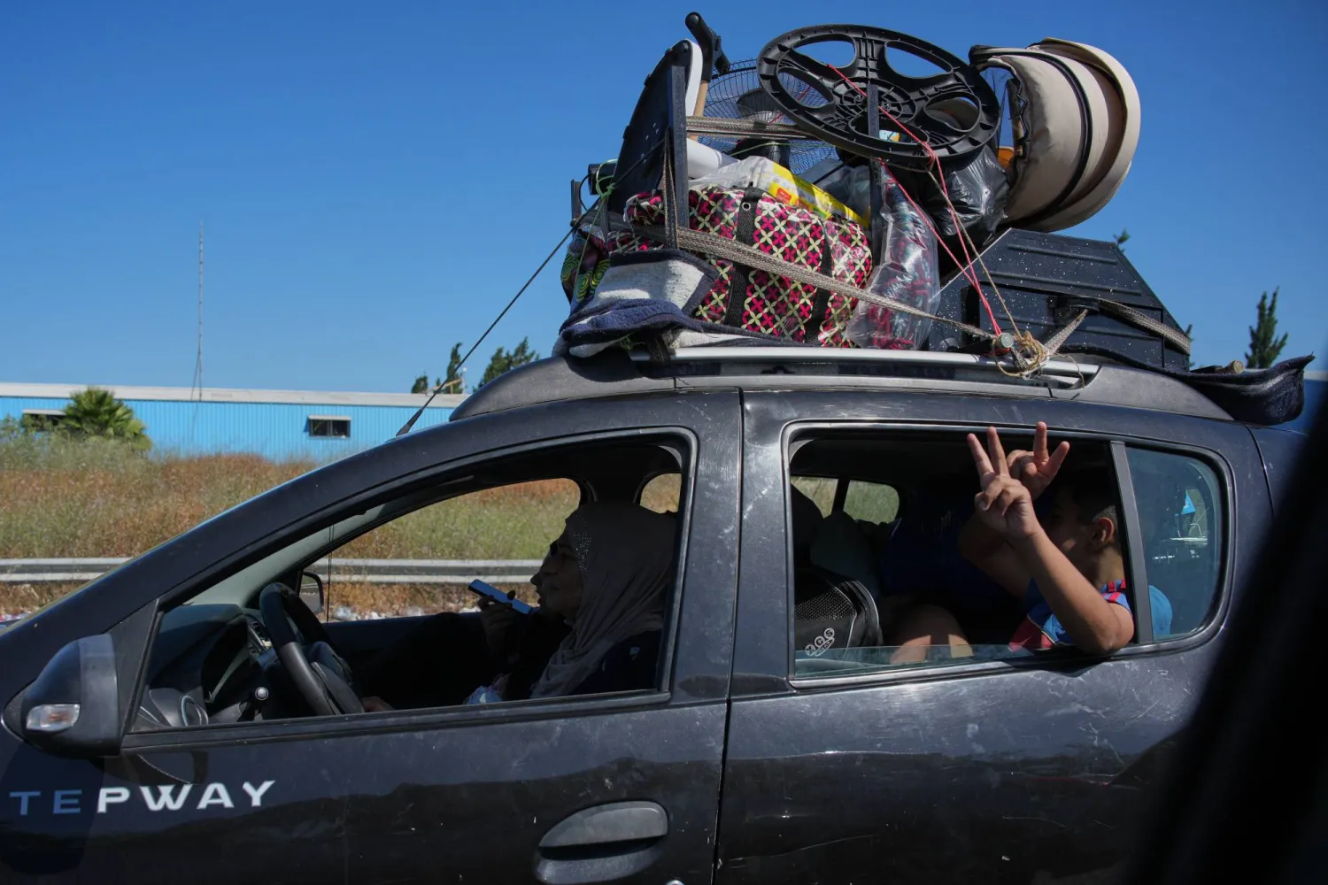 A child flashes a victory sign as he and his family return to their village with their belongings on a highway near the southern port city of Tyre, Lebanon, Thursday, June 18, 2026. (AP Photo/Hassan Ammar)