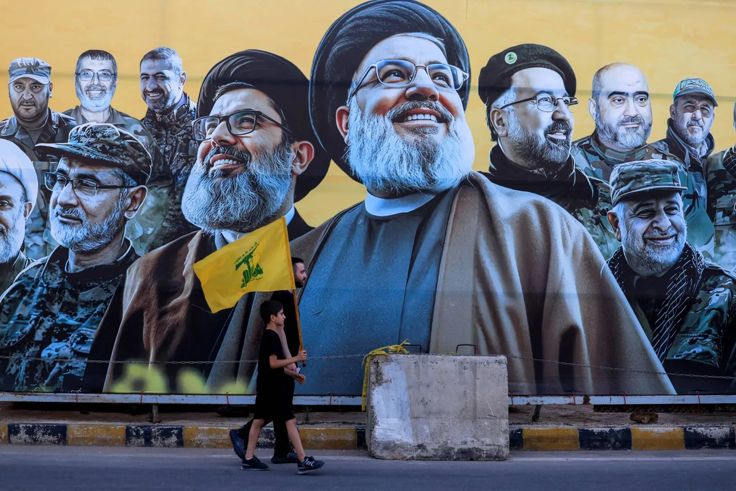 A man walks with a boy, carrying a Hezbollah flag, past a mural depicting former Hezbollah leader Hassan Nasrallah and other senior figures near the burial site of Hassan Nasrallah on the outskirts of Beirut, Lebanon, June 17, 2026. REUTERS/Mohamed Azakir