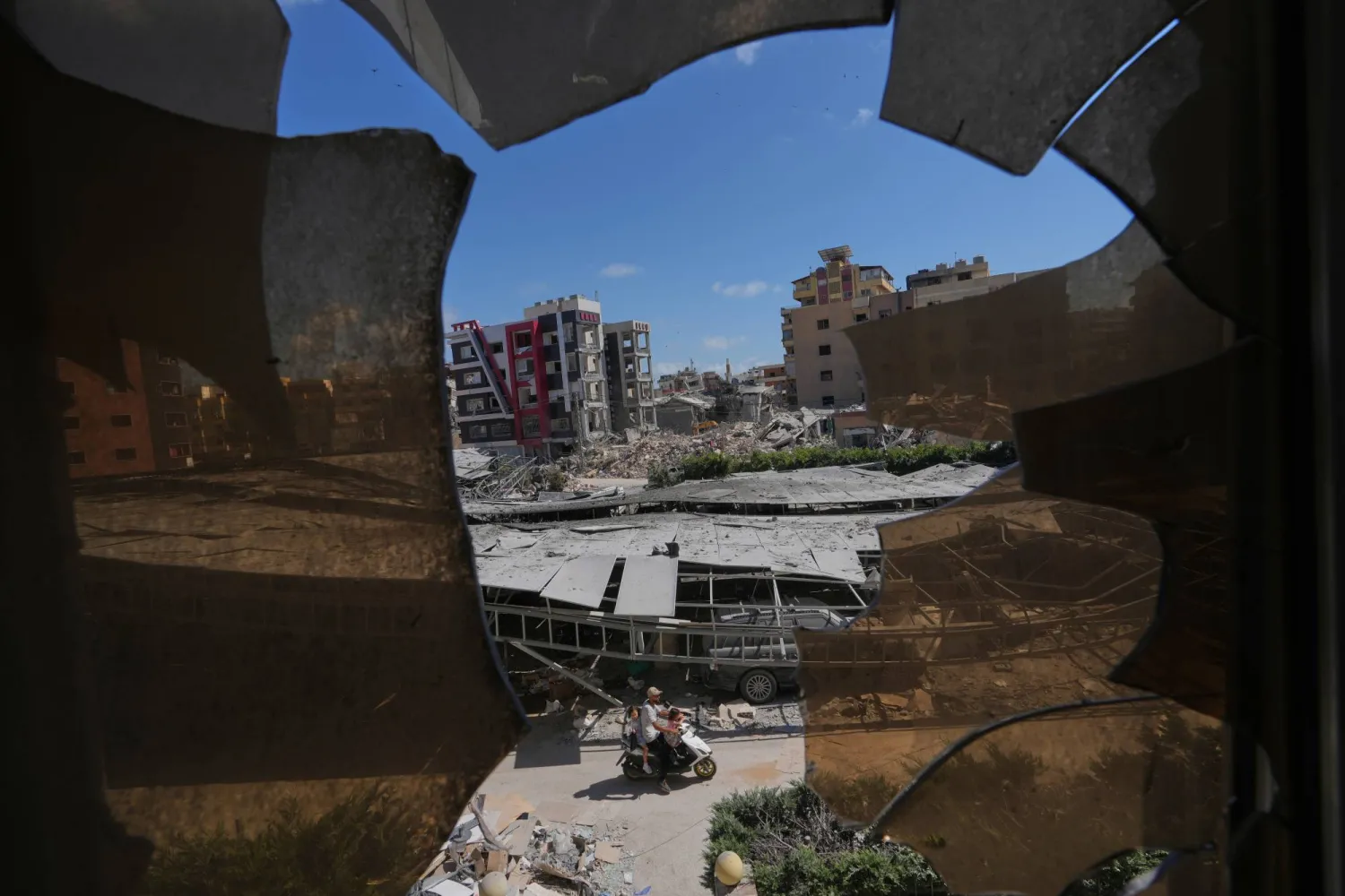 Buildings damaged by Israeli strikes are seen through shattered glass from the Jabal Amel Hospital in the southern port city of Tyre, Lebanon, Thursday, June 18, 2026. (AP Photo/Hassan Ammar)