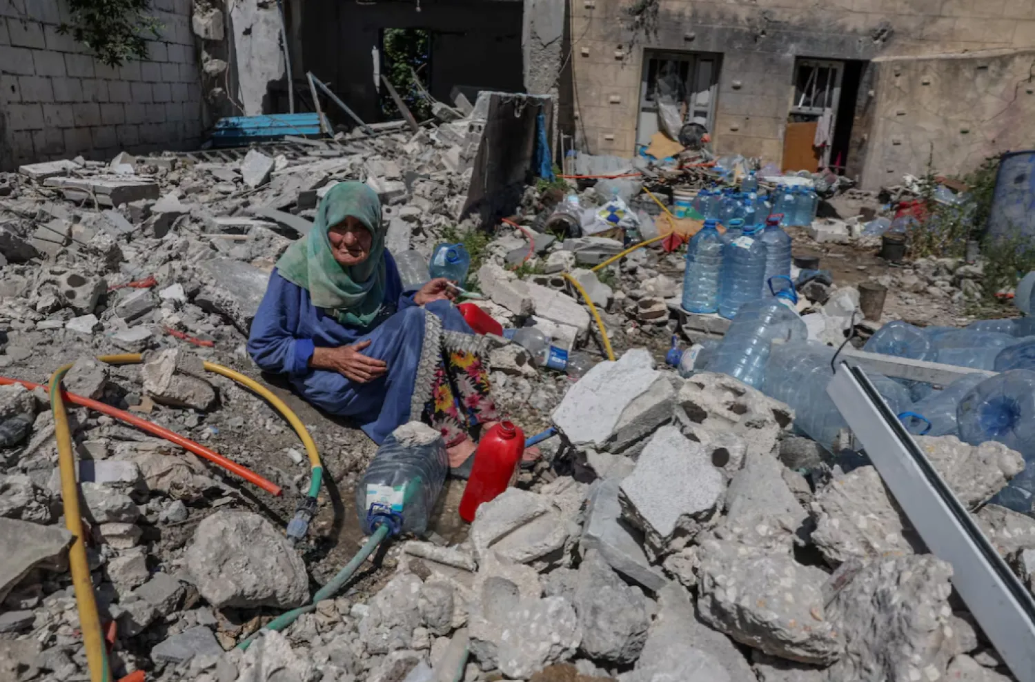 Khadija Amara, whom local residents said had not left her home, fills a jerrycan with water as she sits among the rubble of a house, which was damaged by an Israeli strike, in Qlaileh in the Tyre district, southern Lebanon, June 19, 2026. REUTERS/Zohra Bensemra