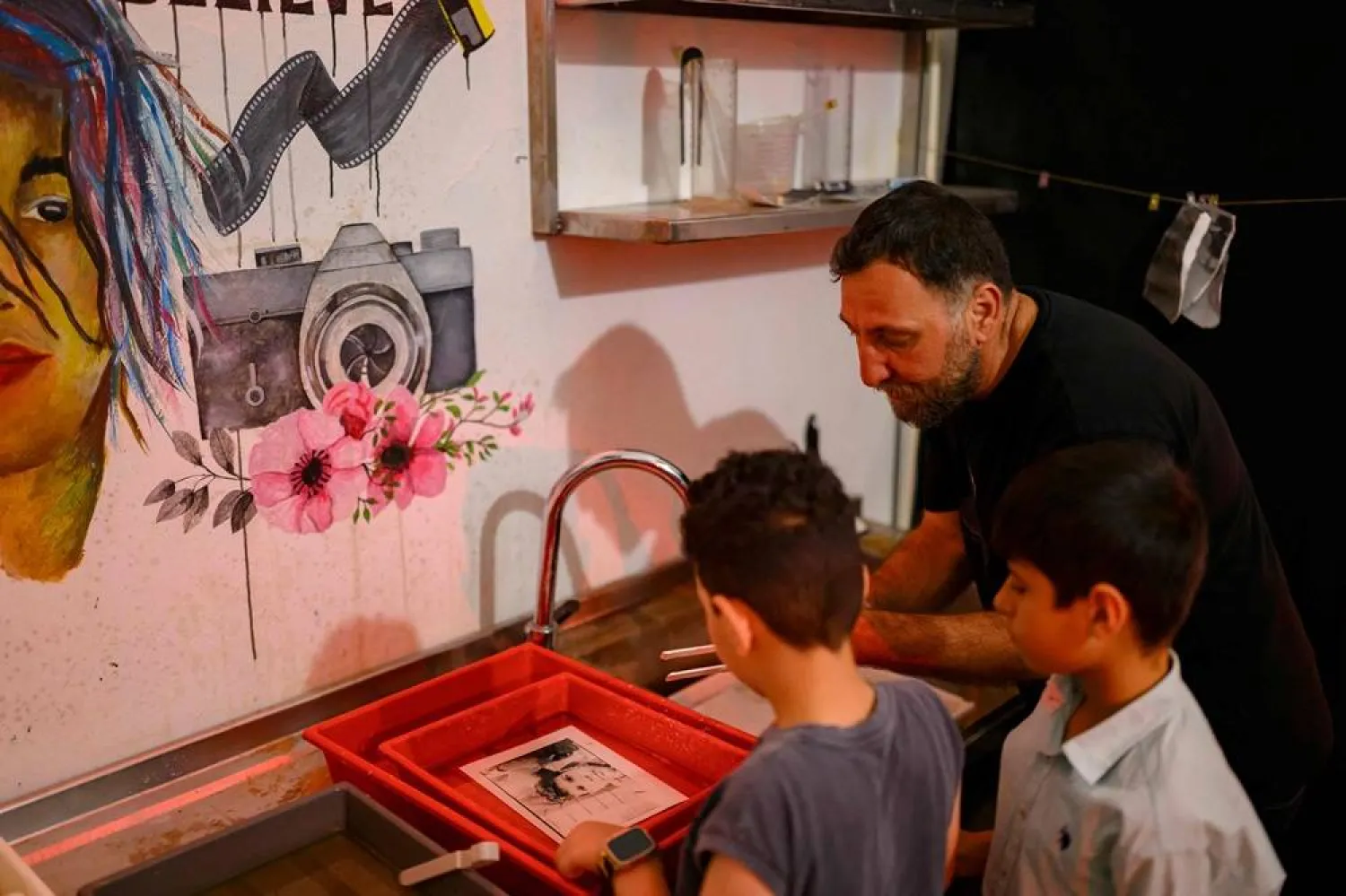 Children work in a darkroom with co-founder of the project, photographer and educator Amar Kilic (R) during a workshop held as part of Fotohane Darkroom project in Mardin, southeastern Türkiye, on June 14, 2026. (AFP)