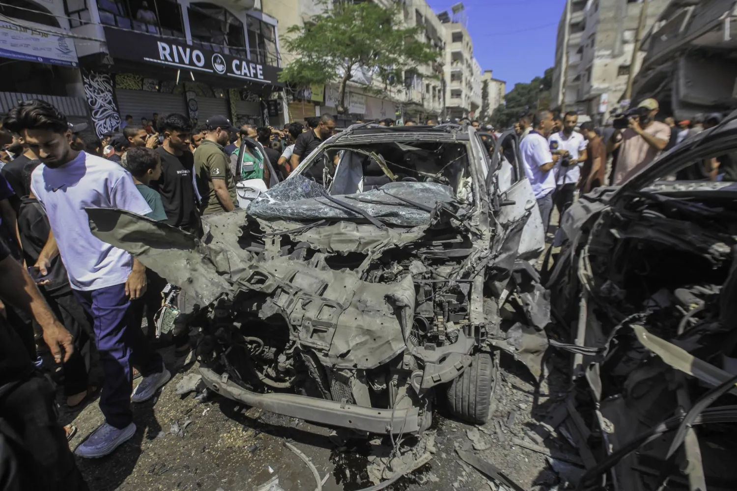 فلسطينيون يتفقدون سيارة استهدفتها طائرات إسرائيلية مسيّرة في حي الرمال في غزة (د.ب.أ)