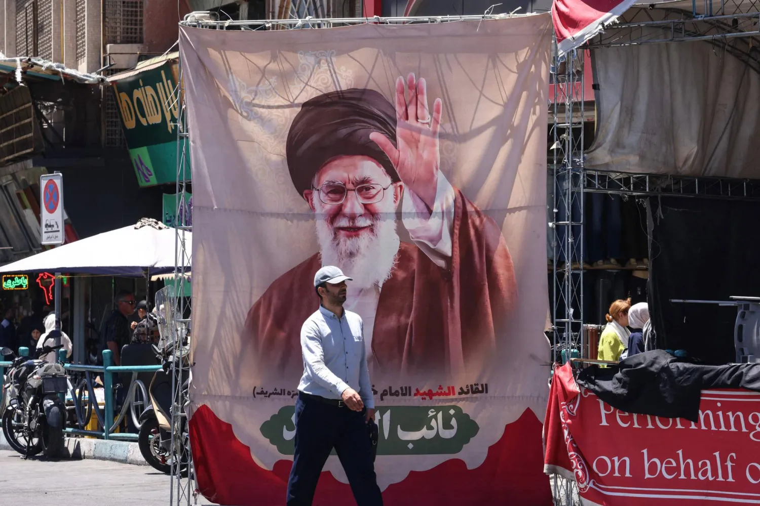 An Iranian man walks past a banner depicting slain supreme leader Ali Khamenei at Valiasr Square in Tehran on June 15, 2026. (AFP)