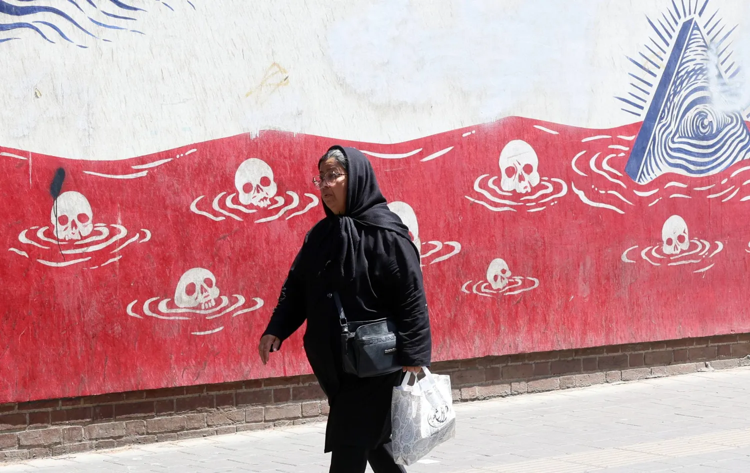 An Iranian woman walks past an anti-US mural next to the former US embassy in Tehran, Iran, 22 June 2026. (EPA)
