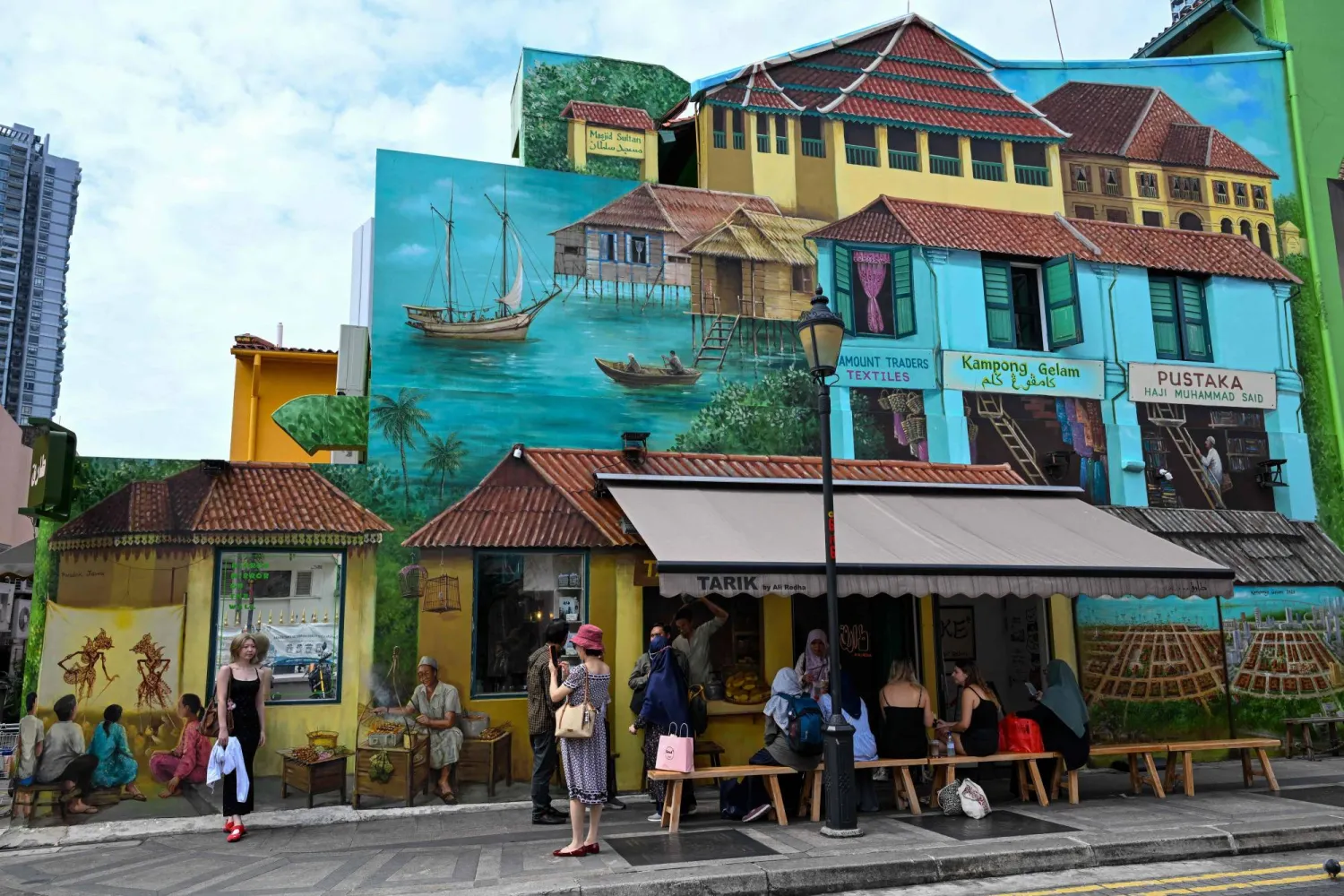 People stop by a cafe with murals painted on its facade in the Arab Street district of Singapore on June 16, 2026. (Photo by Roslan RAHMAN / AFP)