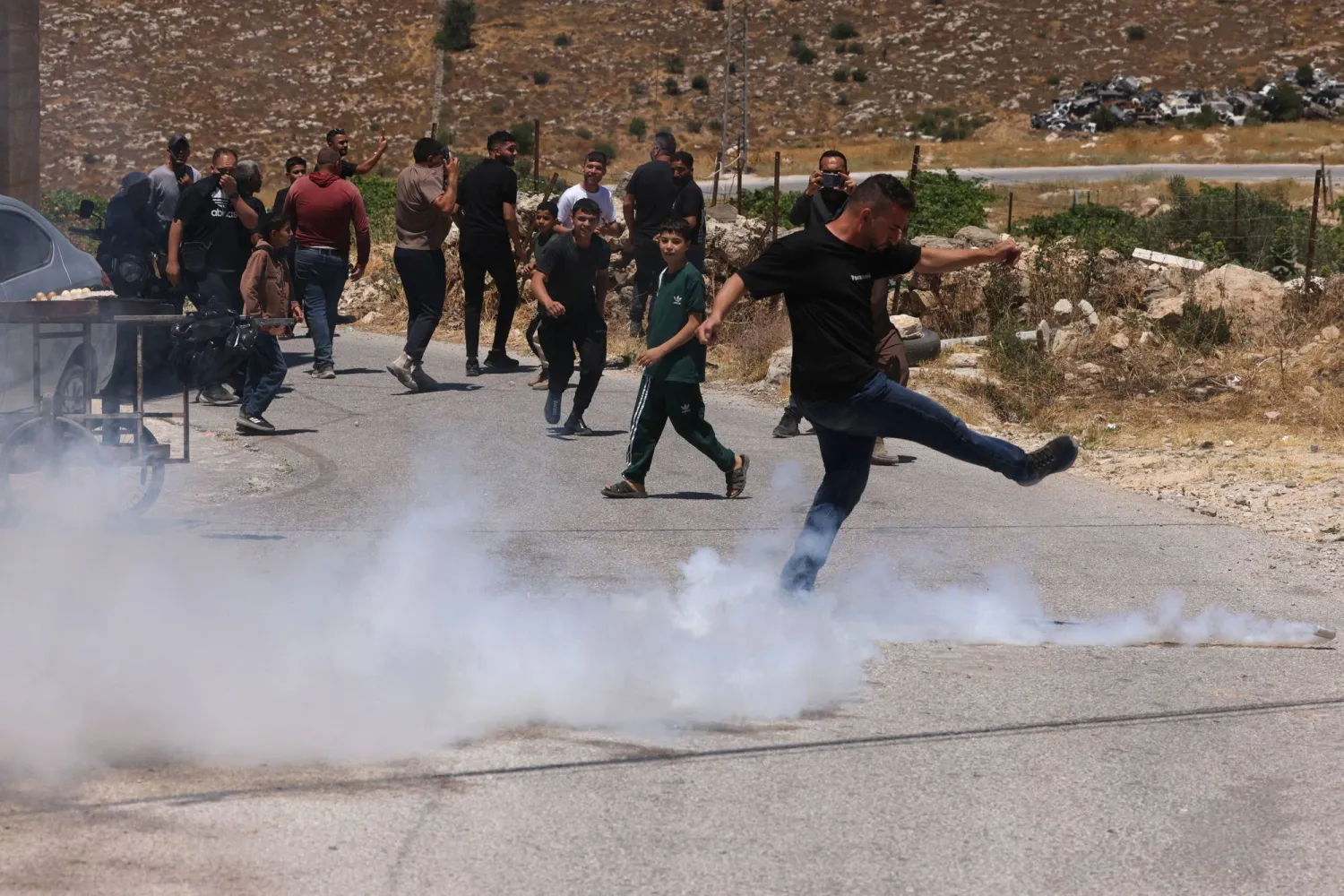 A Palestinian kicks away a teargas cyclinder fired by Israeli security forces guarding bulldozers demolishing the home and shops belonging to the al-Atrash family just south of the Israeli-occupied West Bank city of Hebron on June 23, 2026. (Photo by HAZEM BADER / AFP)