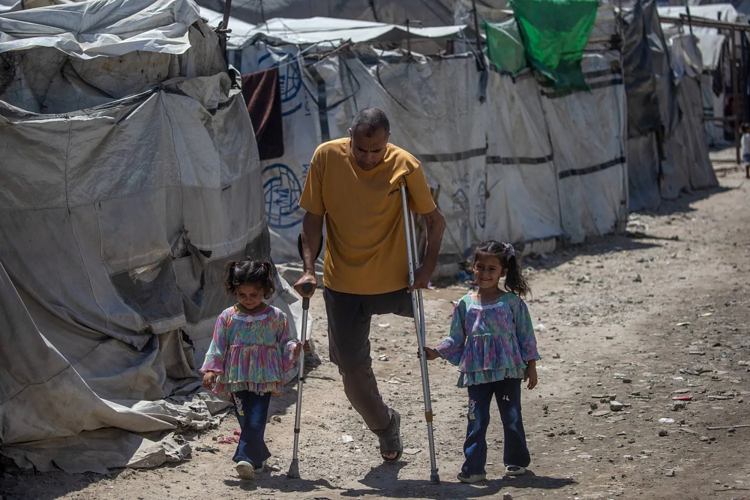فلسطيني محرر من السجون الإسرائيلية مبتور الساق يسير مع ابنتيه في مخيم للنازحين بمدينة غزة (إ.ب.أ)