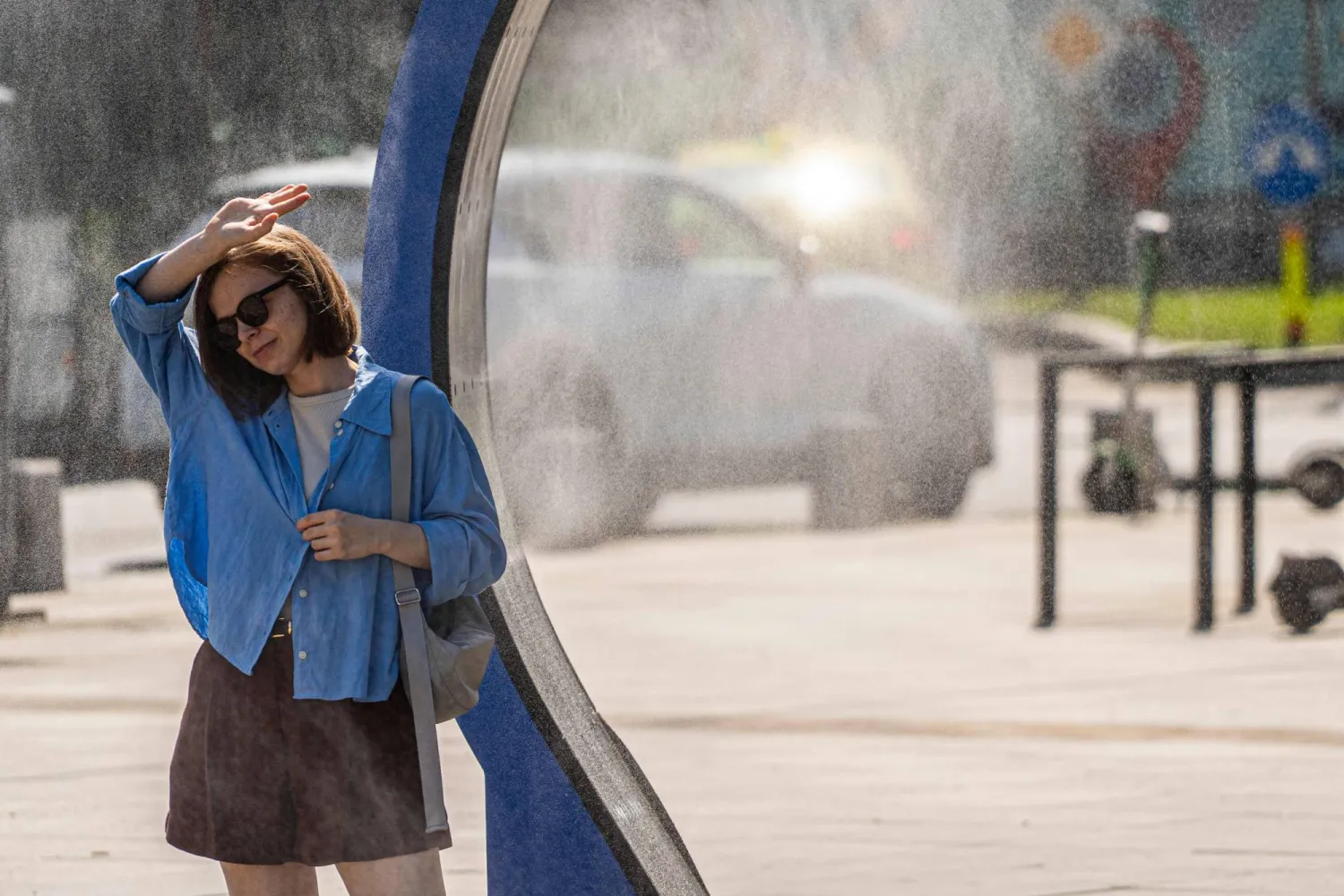 A woman cools off while walking through a water sprayer installed in central Bucharest, on June 28, 2026. (Photo by Mihai Barbu / AFP)