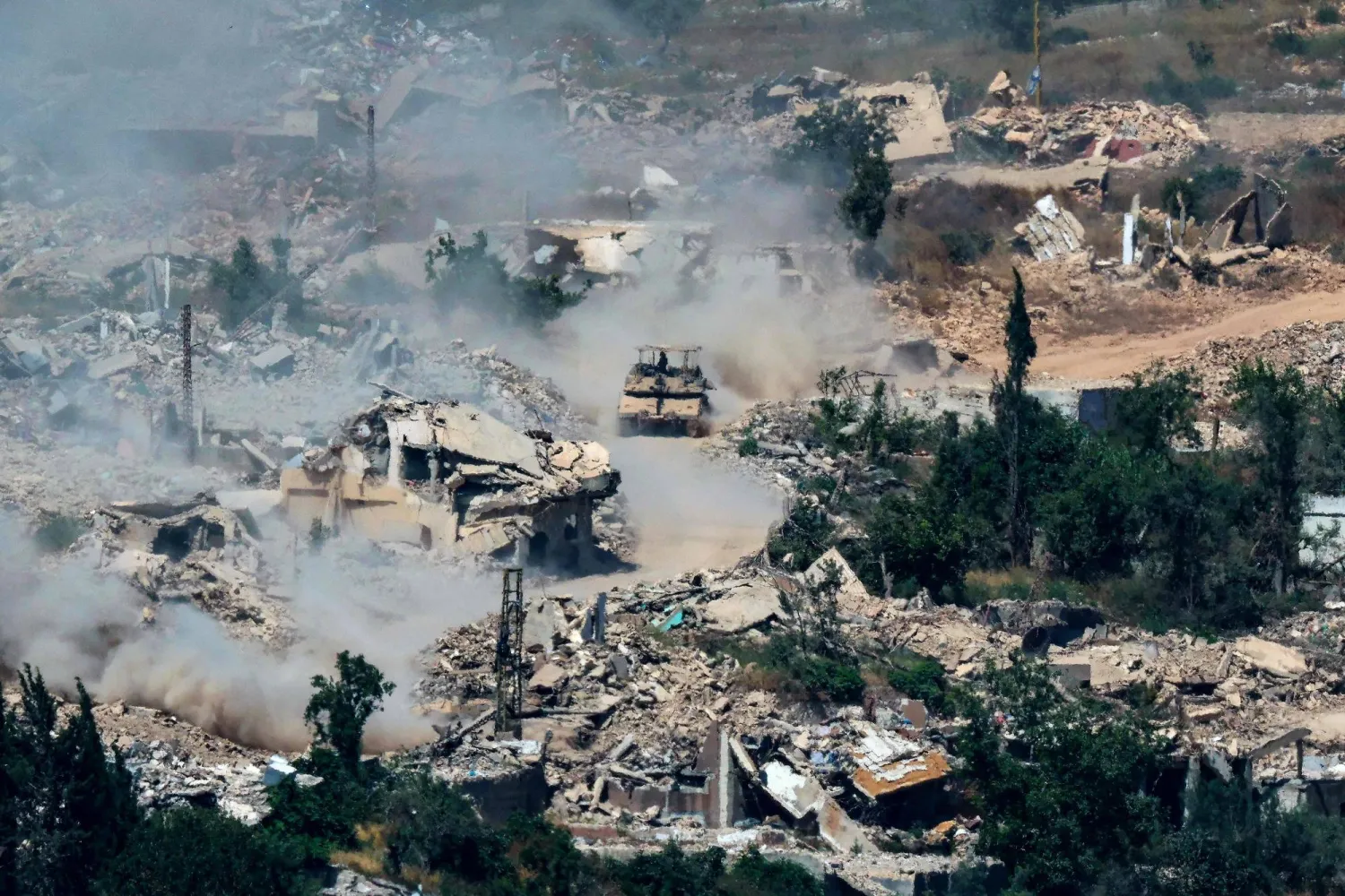 This picture taken from a position in the Upper Galilee in northern Israel, near the Israel-Lebanon border shows Israeli Merkava tanks driving along a road past destroyed buildings in southern Lebanon on June 17, 2026. (Photo by JACK GUEZ / AFP)