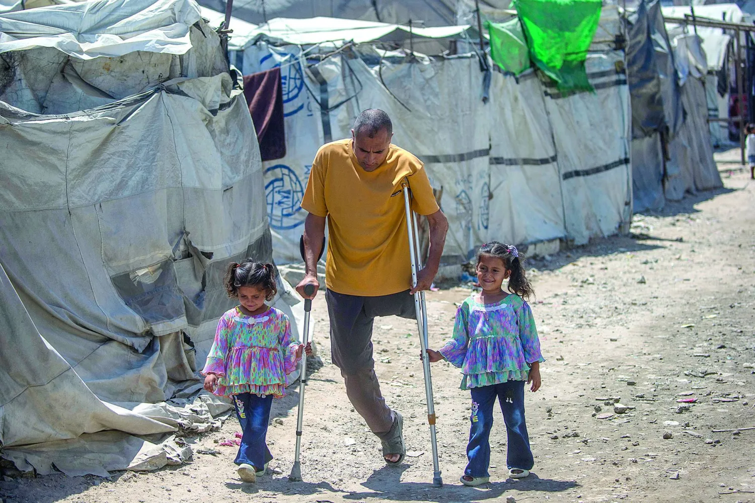 
فلسطيني محرَّر من السجون الإسرائيلية مبتور الساق يسير مع ابنتيه في مخيم للنازحين بمدينة غزة (إ.ب.أ)