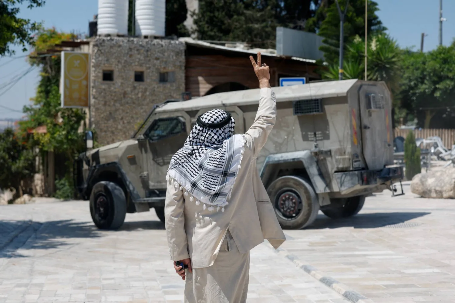 رجل فلسطيني يرفع إشارة النصر إلى جانب آلية عسكرية إسرائيلية، بينما يزور مستوطنون إسرائيليون وقوات من الجيش الإسرائيلي الموقع الأثري في سبسطية بالضفة الغربية المحتلة (رويترز)