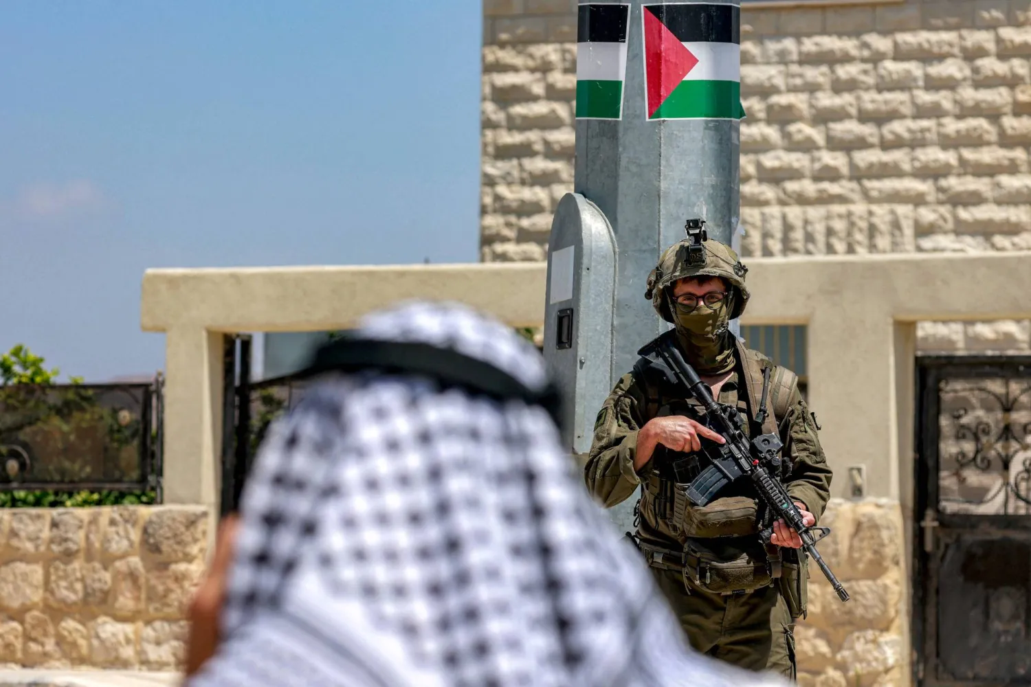 فلسطيني يتحدث عبر الهاتف بالقرب من جندي إسرائيل في موقع أثري بسبسطية شمال نابلس بالضفة الغربية المحتلة يوم الاثنين (أ.ف.ب)