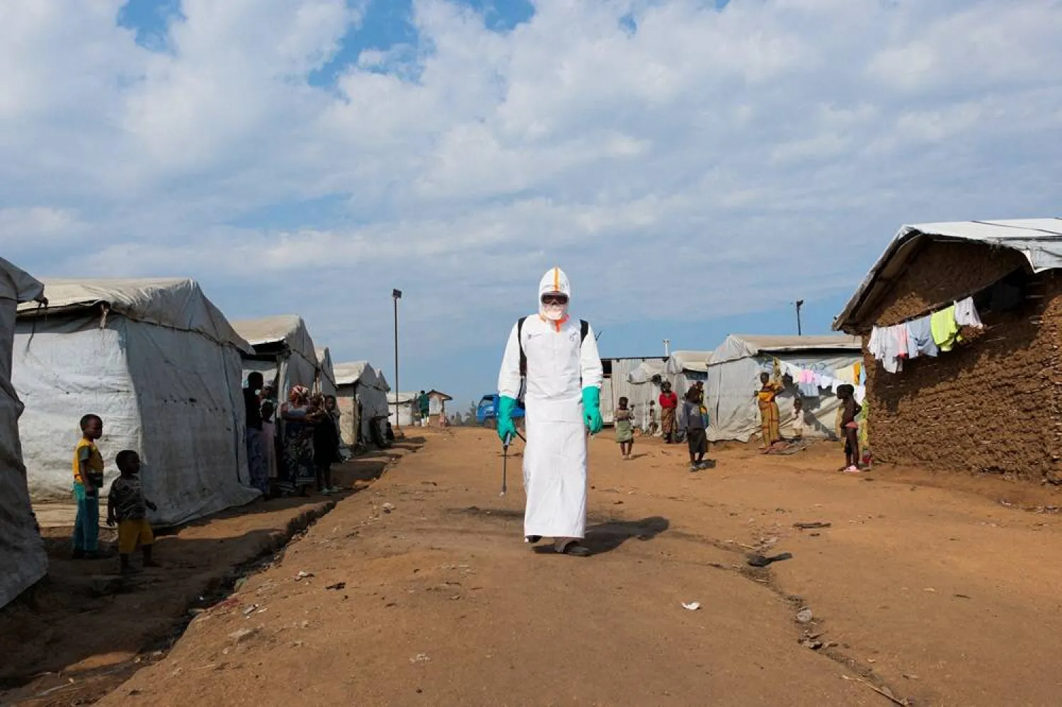 Displaced people watch a health worker in full personal protective equipment (PPE) preparing to disinfect the area during the burial of suspected Ebola victims at the Kigonze displaced persons camp in Bunia, eastern Democratic Republic of Congo, on June 18, 2026, one month after the outbreak was declared. (Reuters)