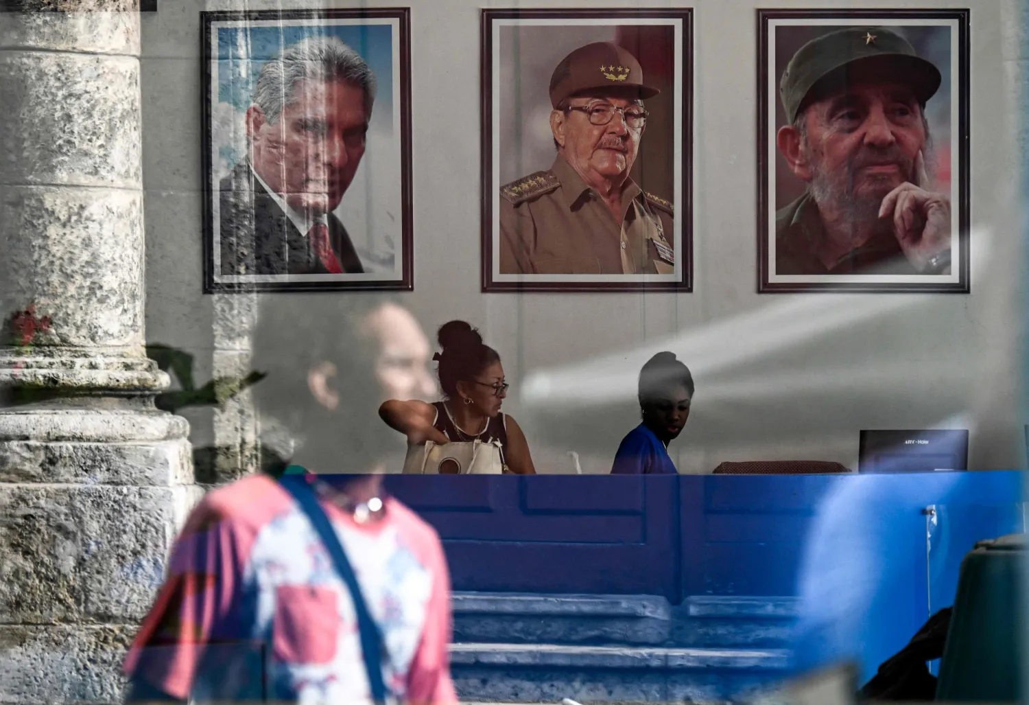 People are seen through a window beneath framed portraits of (L to R) Cuba's President Miguel Diaz-Canel, former president Raul Castro and late leader Fidel Castro, in Havana on June 5, 2026. (Photo by YAMIL LAGE / AFP)