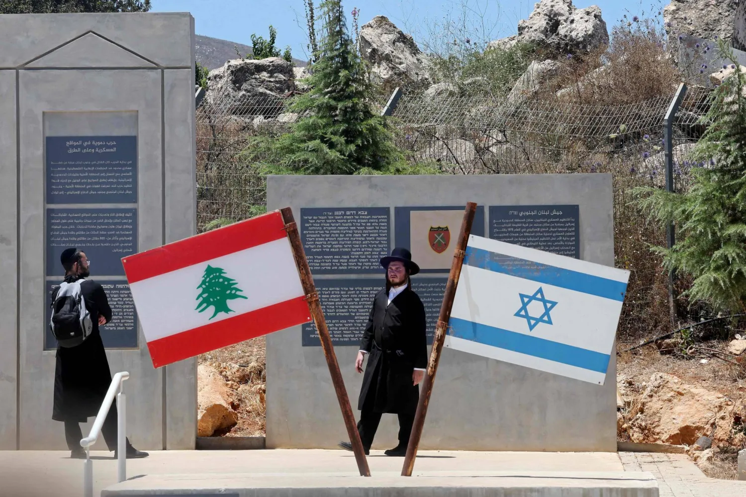 يهودان من طائفة «الحريديم» (المتشددين دينياً) يقفان بجوار العلمين الإسرائيلي واللبناني في موقع عند الحدود مع لبنان في شمال إسرائيل (أ.ف.ب)
