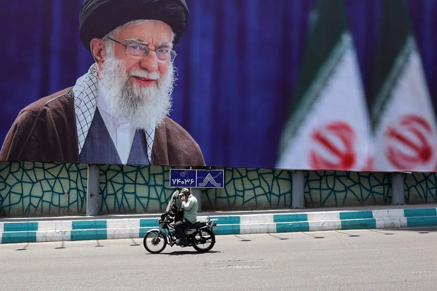 An Iranian man rides a motorbike past a large-scale poster of late Iranian Supreme Leader Ali Khamenei displayed along a highway, in Tehran, Iran, 01 July 2026. (Reuters)