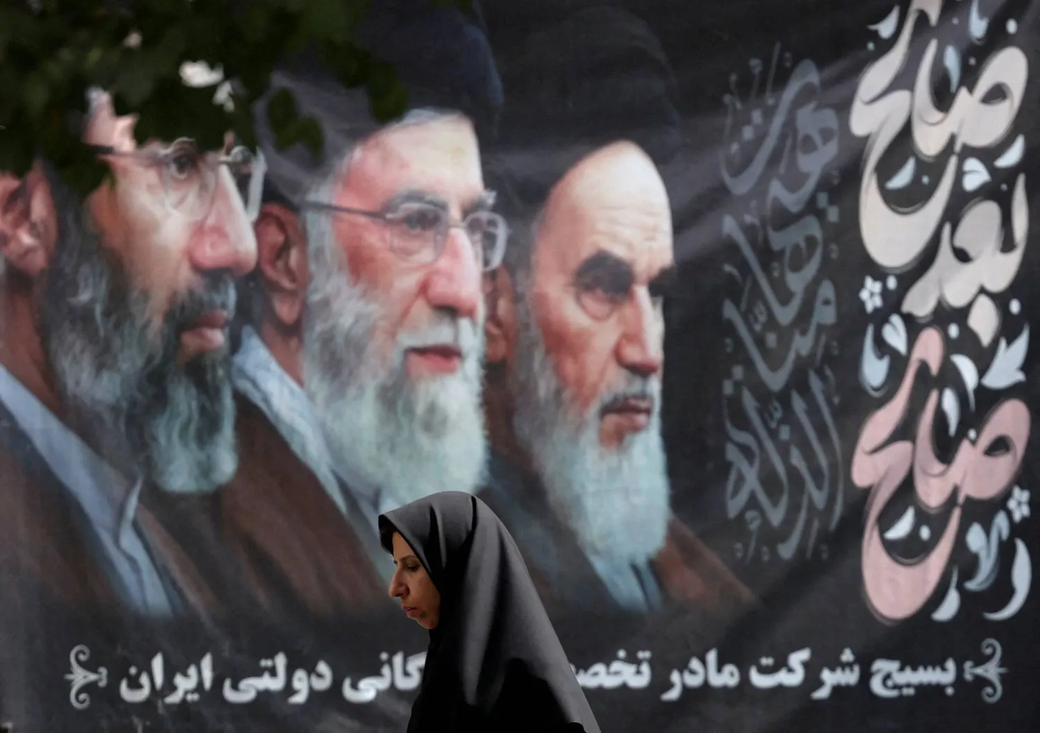 امرأة تمر بجوار ملصق يحمل صور المرشد الأعلى الإيراني السابق علي خامنئي في أحد شوارع طهران (رويترز)
