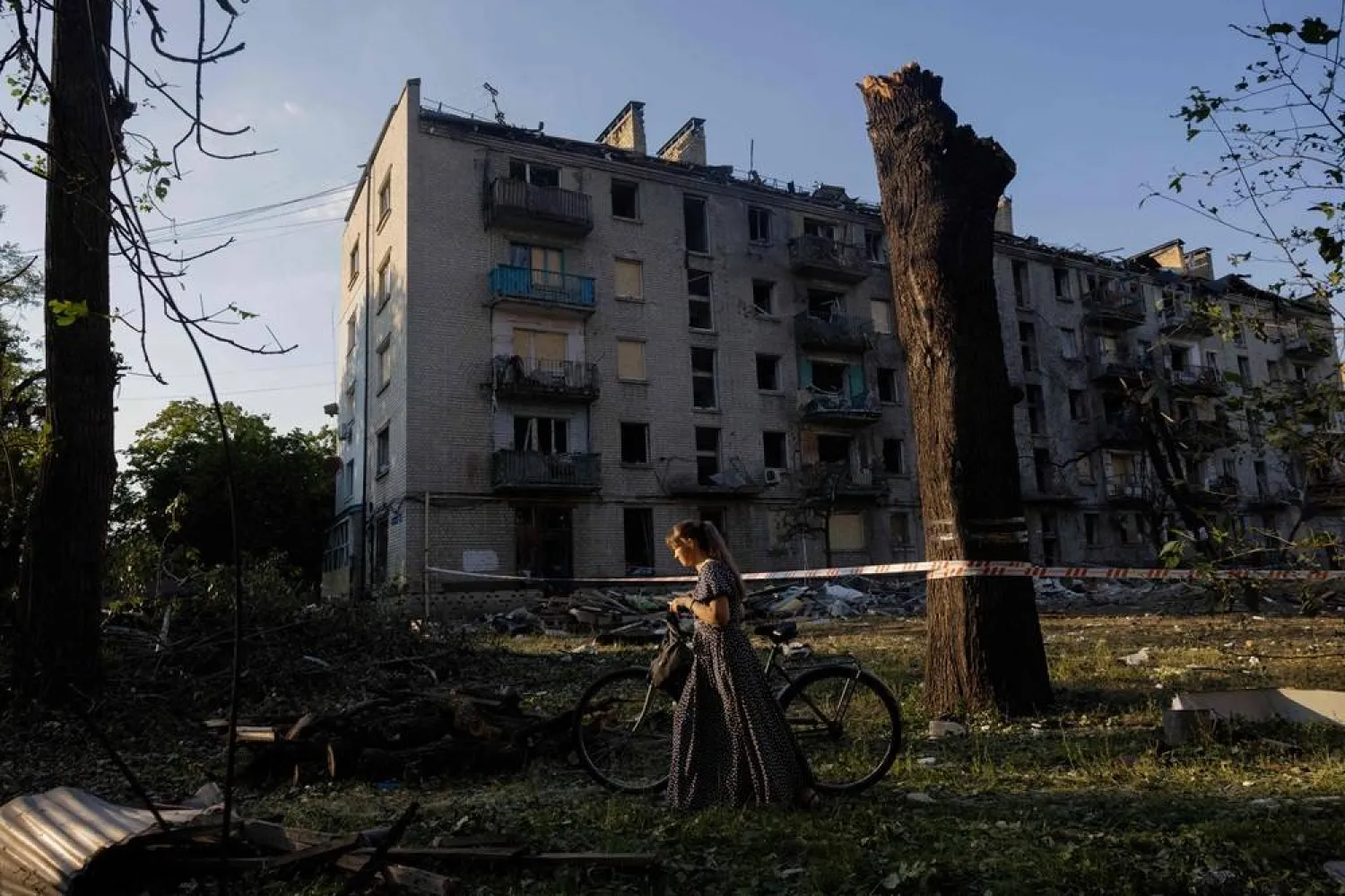 A woman with a bicycle walks by a residential building damaged following a Russian air attack on the Ukrainian capital of Kyiv on July 2, 2026, (AFP)