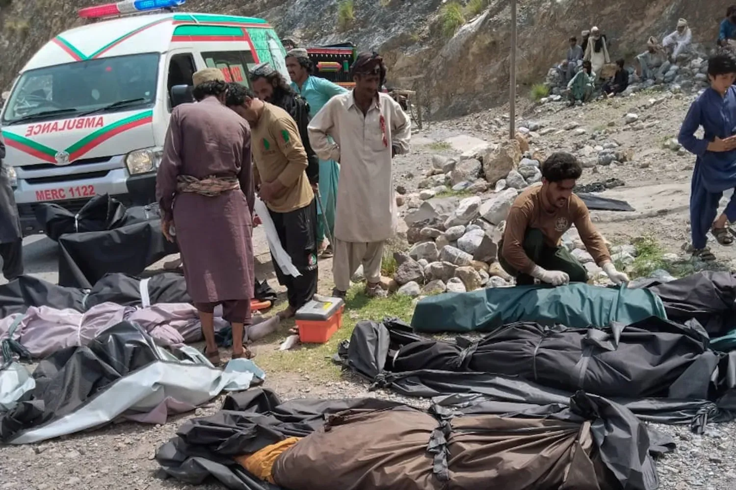 Pakistan'ın güneybatısında, Belucistan ile Hayber Pahtunhva eyaletleri sınırına yakın, ulaşımı güç Dana Sar bölgesinde yolcu otobüsünün otoyoldan çıkarak kayalık vadiye yuvarlanmasının ardından cesetleri çıkarılan kurbanların üzeri, kurtarma ekipleri ve gönüllüler tarafından örtülüyor. (AP, 3 Temmuz 2026)