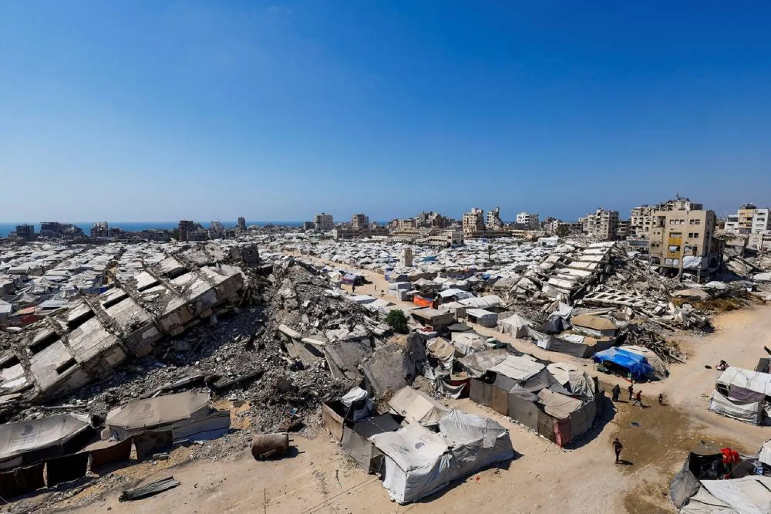  Palestinians make their way past the rubble of residential buildings destroyed during the Israeli offensive as displaced people shelter in tents, in Gaza City, July 4, 2026. (Reuters)