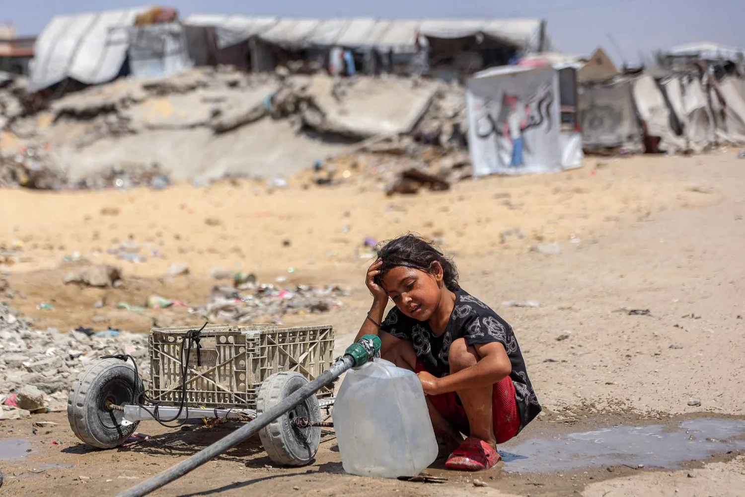 فتاة فلسطينية تملأ أوعيةً بالماء المستخرج من بقايا أنابيب تحت الأرض بمخيم للنازحين جراء الحرب في حي الشيخ رضوان بمدينة غزة (أ.ف.ب)