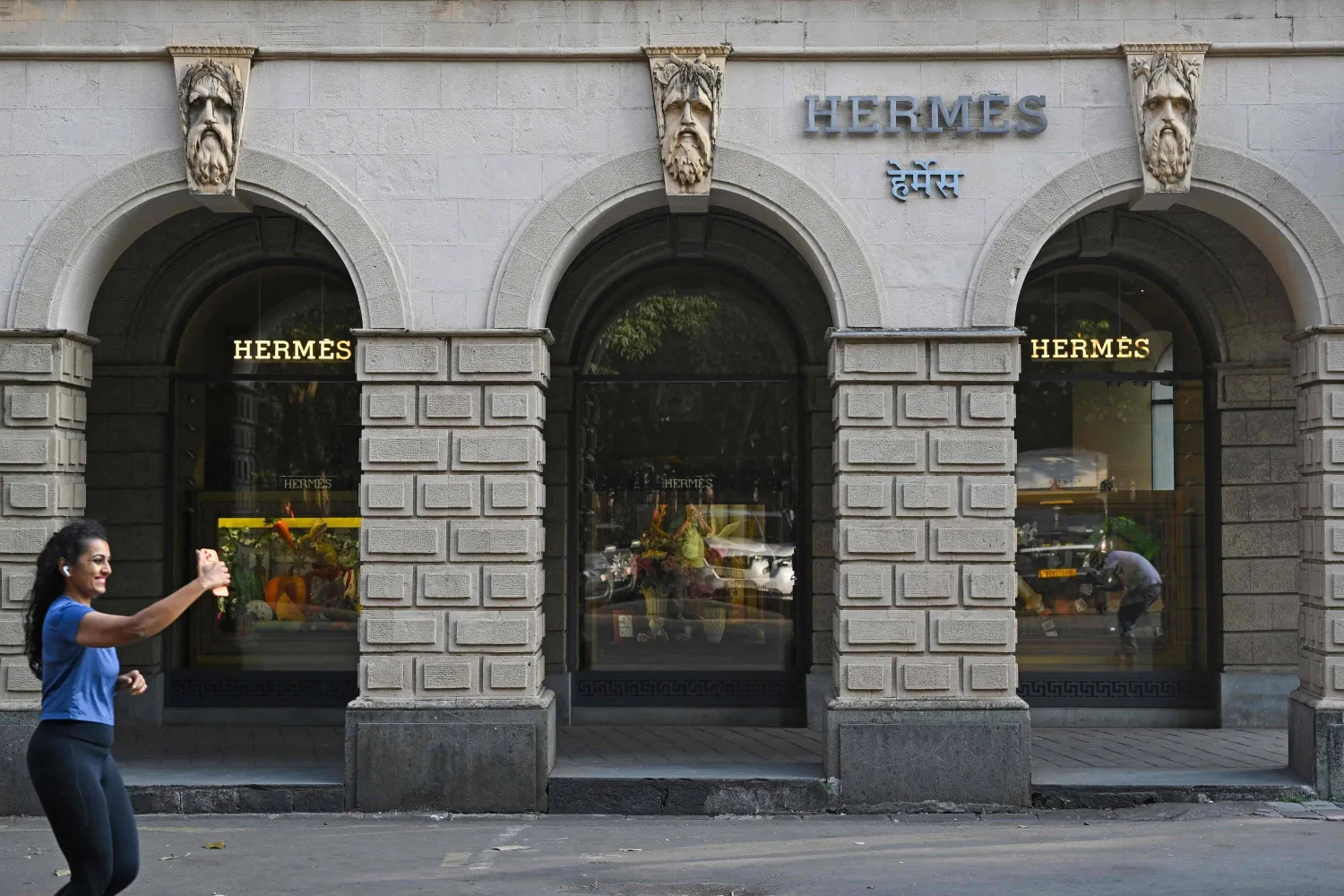 A woman makes a reel while running past the French luxury brand Hermes store, Mumbai, India, Nov. 14, 2025. (AFP) 