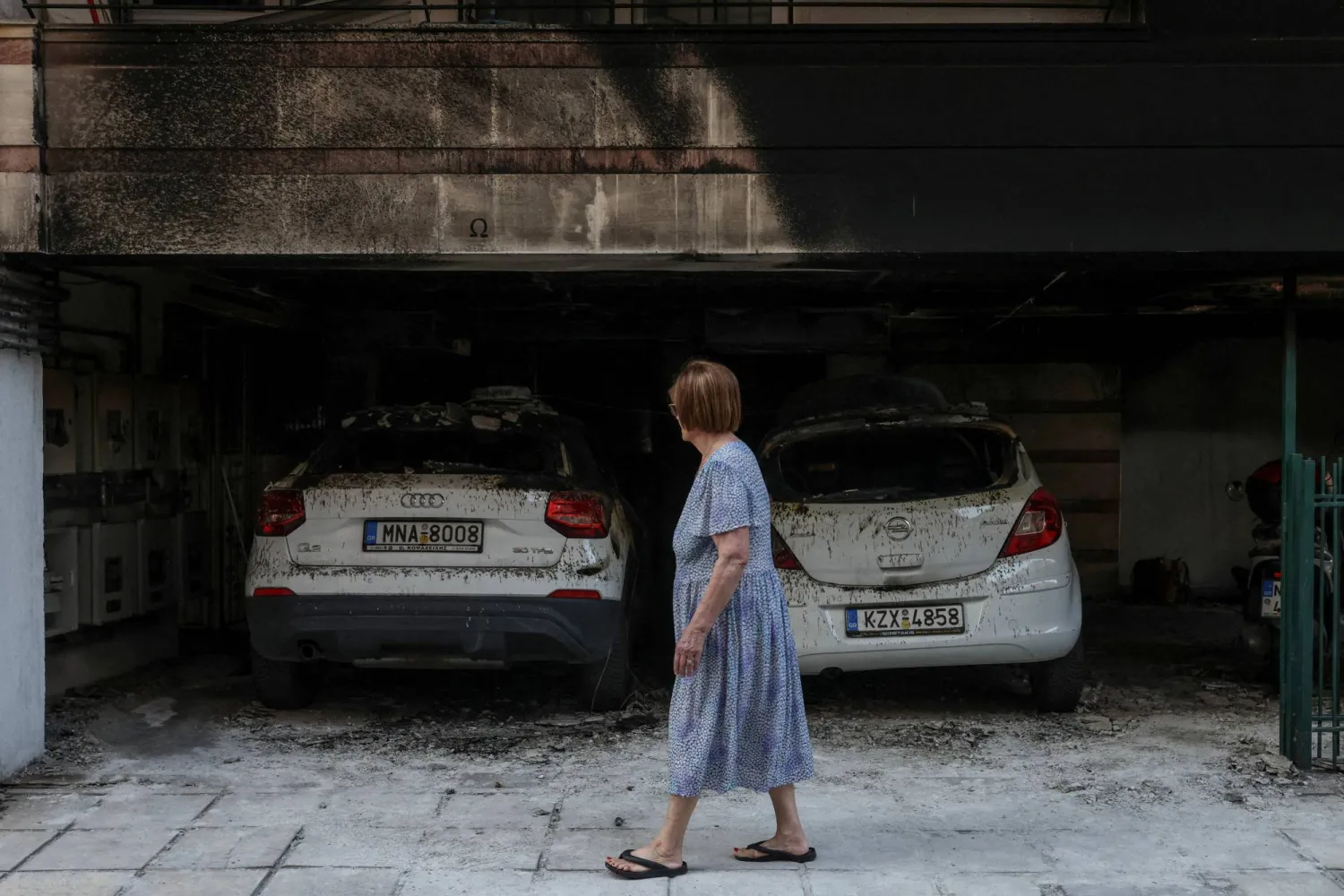 FILE PHOTO: A woman walks past damaged cars and a building after attackers firebombed three residential buildings linked to Greece's governing party in the northern city of Thessaloniki, Greece, July 1, 2026. REUTERS/Alexandros Avramidis/File Photo