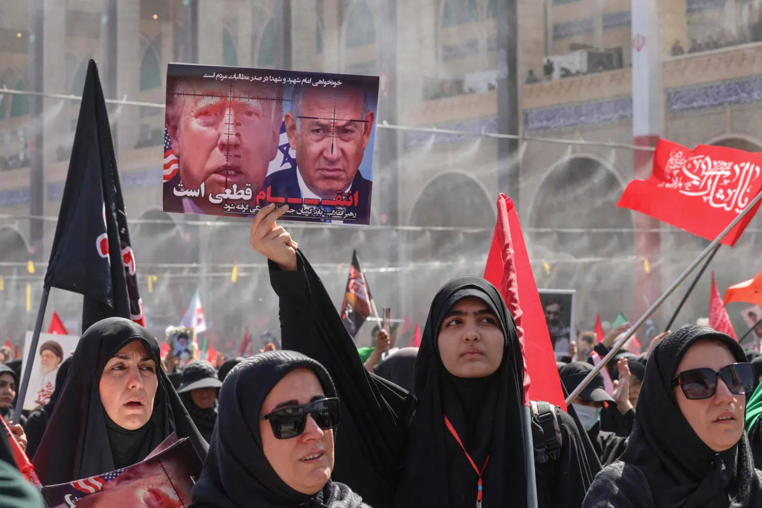 TOPSHOT - A mourner holds up a sign bearing the images of US President Donald Trump and Israel's Prime Minister Benjamin Netanyahu with a phrase reading "Revenge is certain" at the Grand Mosalla where people gathered to pray for Iran's slain supreme leader Ali Khamenei during the second day of funeral ceremonies at the Grand Mosalla in Tehran on July 5, 2026. (Photo by ATTA KENARE / AFP) 