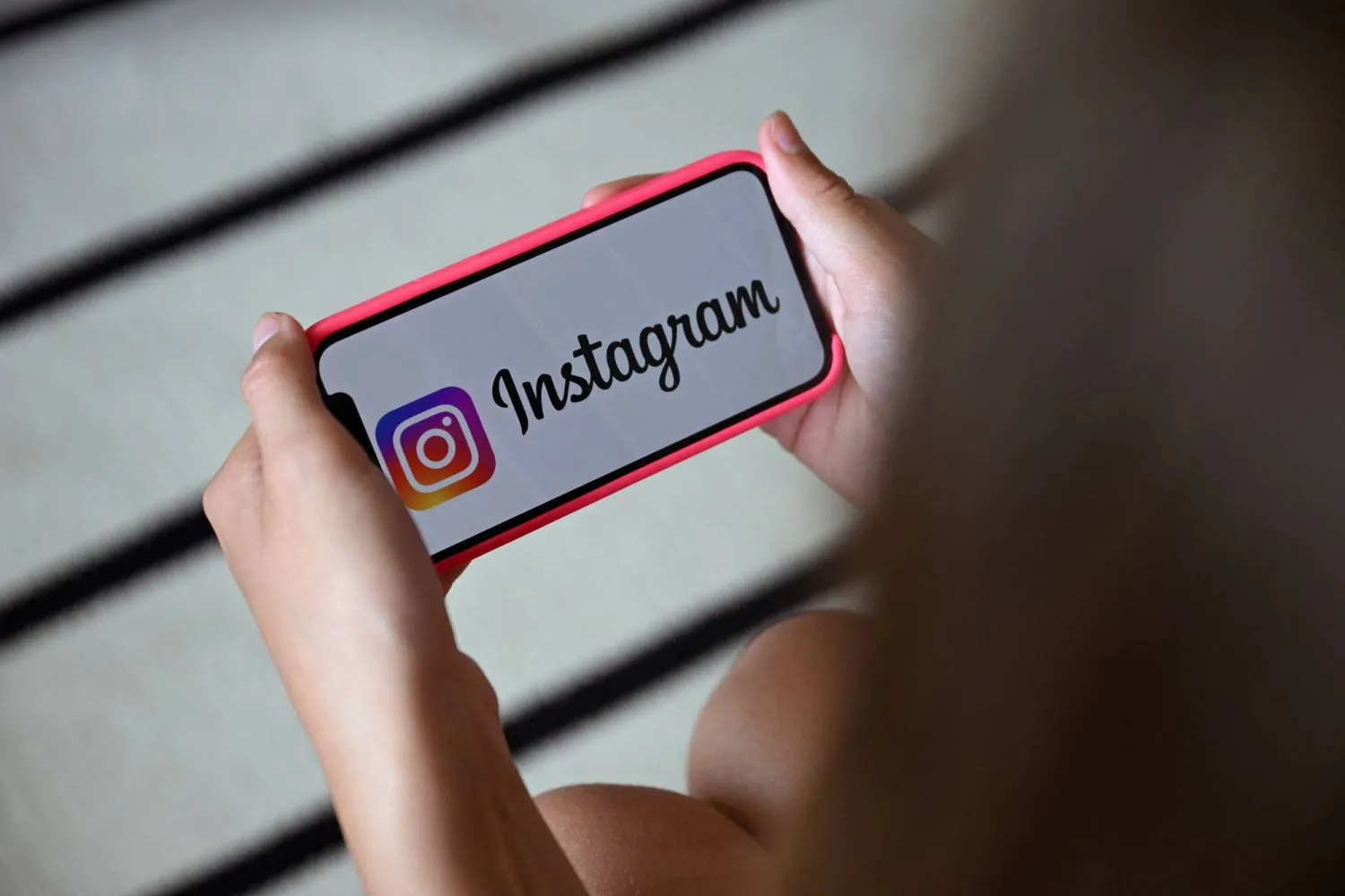 A teenager holds her smartphone displaying the logo of US social network Instagram in Brussels on July 7, 2026. (AFP)