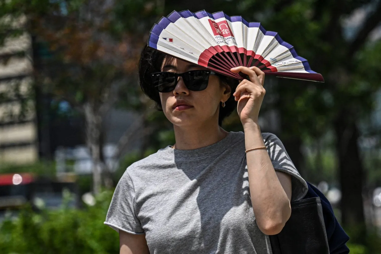 A woman uses a fan to shelter from the sun on a street in Seoul on July 12, 2026. (Photo by JADE GAO / AFP)
