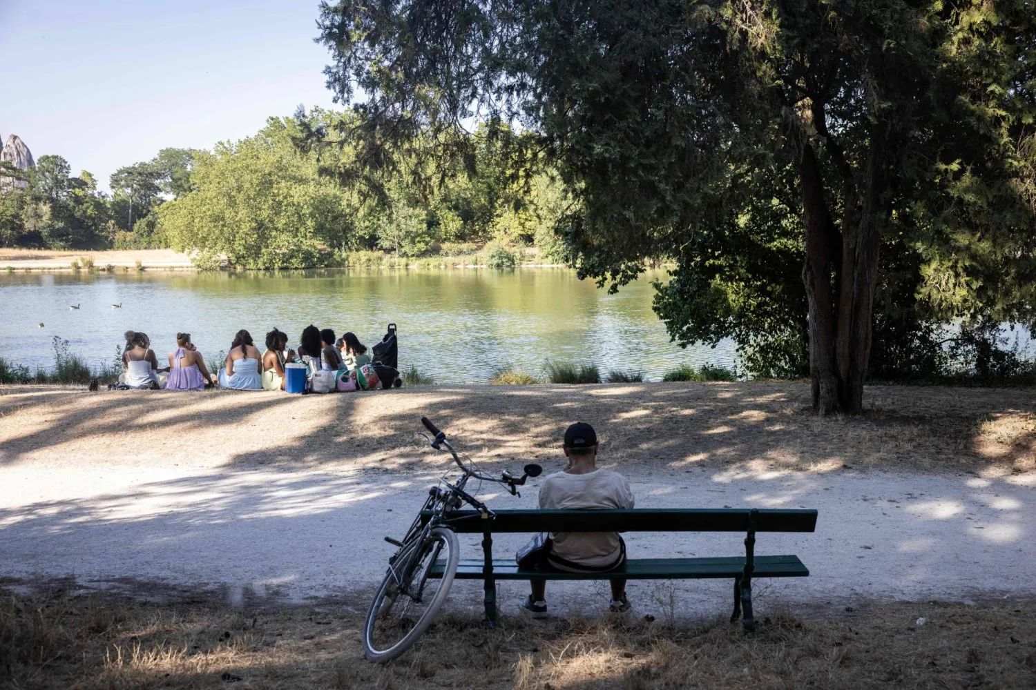 People picnic in the shadow of a tree to protect from the sun during a heatwave by the Daumesnil Lake at the Bois de Vincennes park in Paris on July 11, 2026. (Photo by Behrouz MEHRI / AFP)