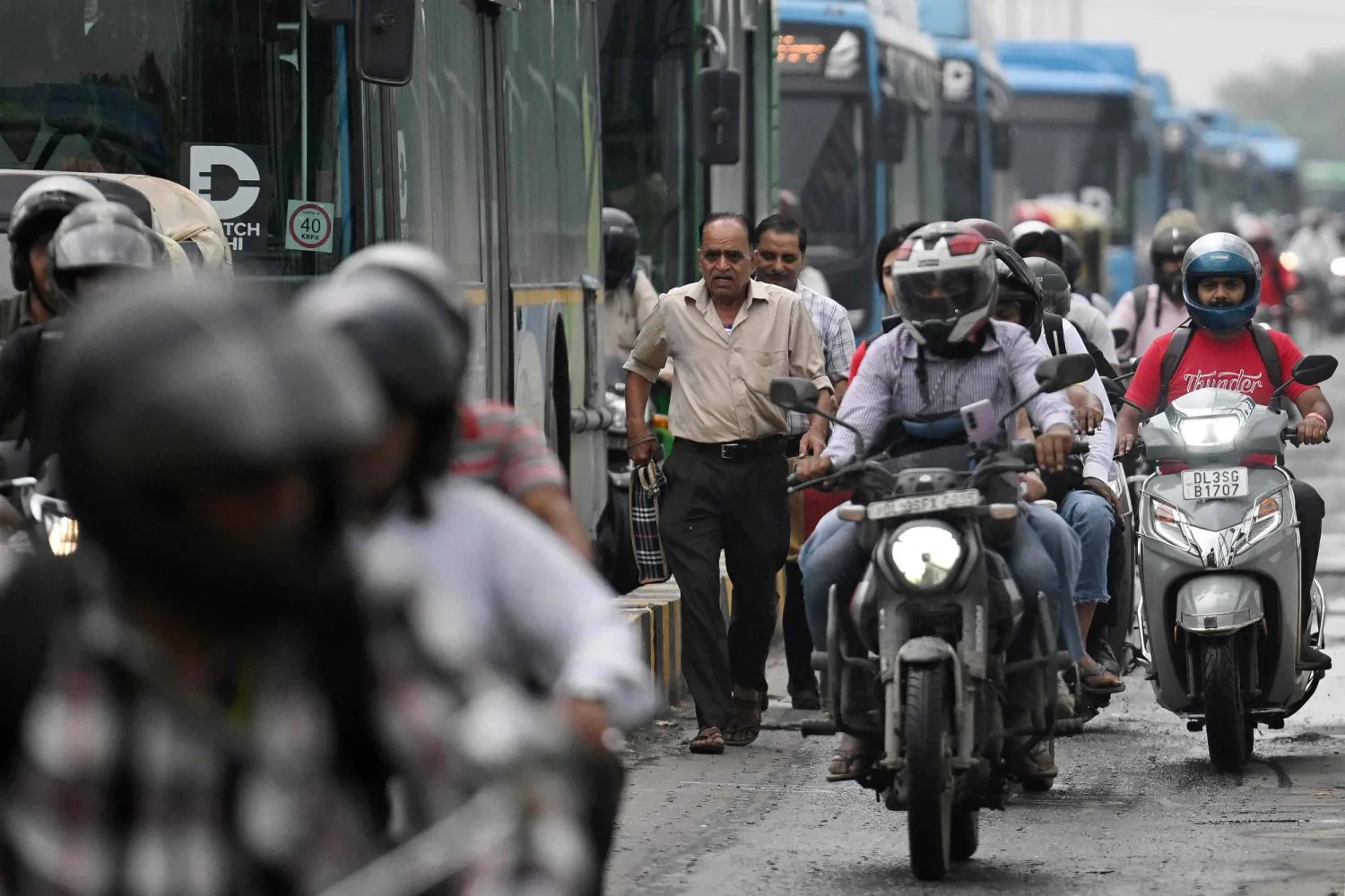 This photograph taken on July 8, 2026 shows a pedestrian (C) walking amidst vehicles along a bridge in New Delhi. (Photo by Arun SANKAR / AFP)