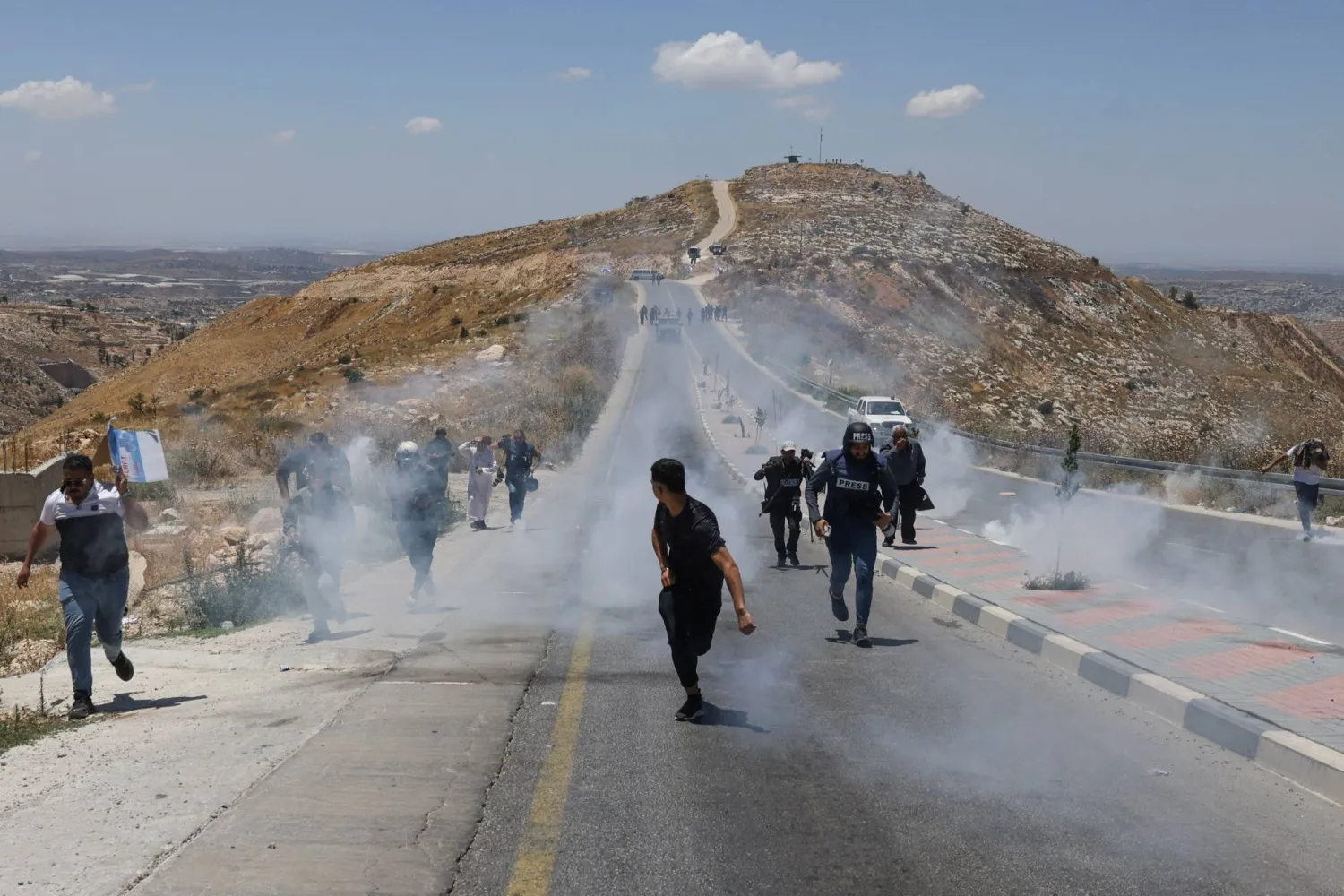 TOPSHOT - Journalists, protesters and local Palestinian landowners, who say some of their land was taken for the newly built Mount Tarousa settlement (background), run from tear gas fired by Israeli security forces blocking a road leading to the hilltop during a rally against the settlement near Dura in the Israeli-occupied West Bank on June 19, 2026. (Photo by HAZEM BADER / AFP)