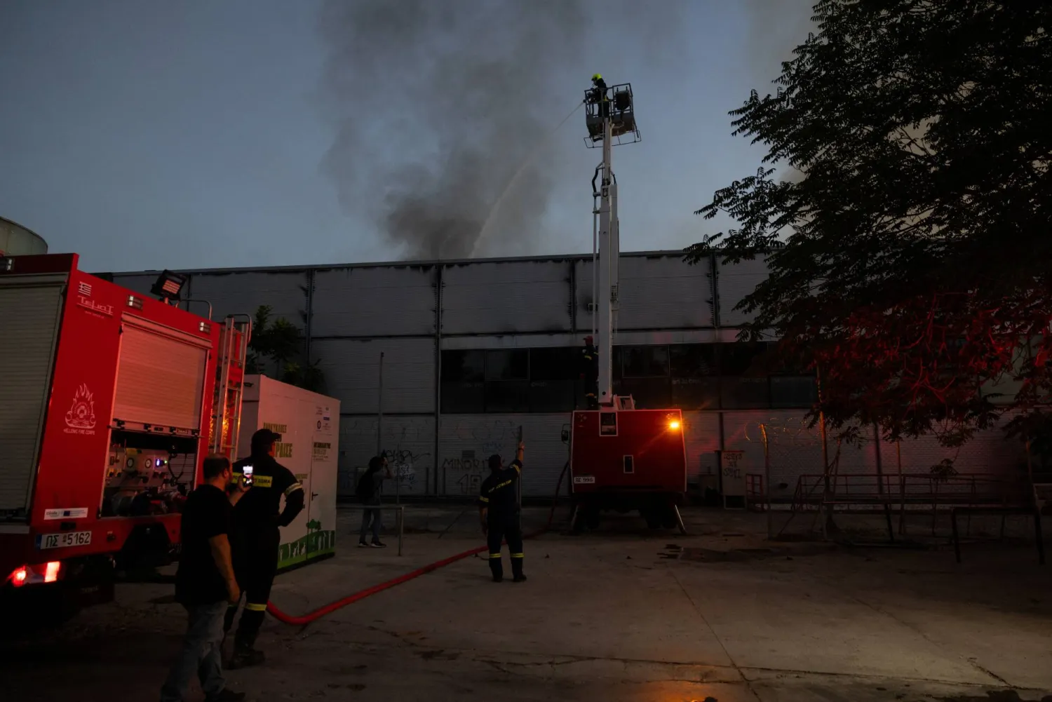 A firefighter sprays water from an aerial platform onto the roof of the Badminton Theater as smoke rises following a fire, in Athens, Greece, July 12, 2026. REUTERS/Stelios Misinas