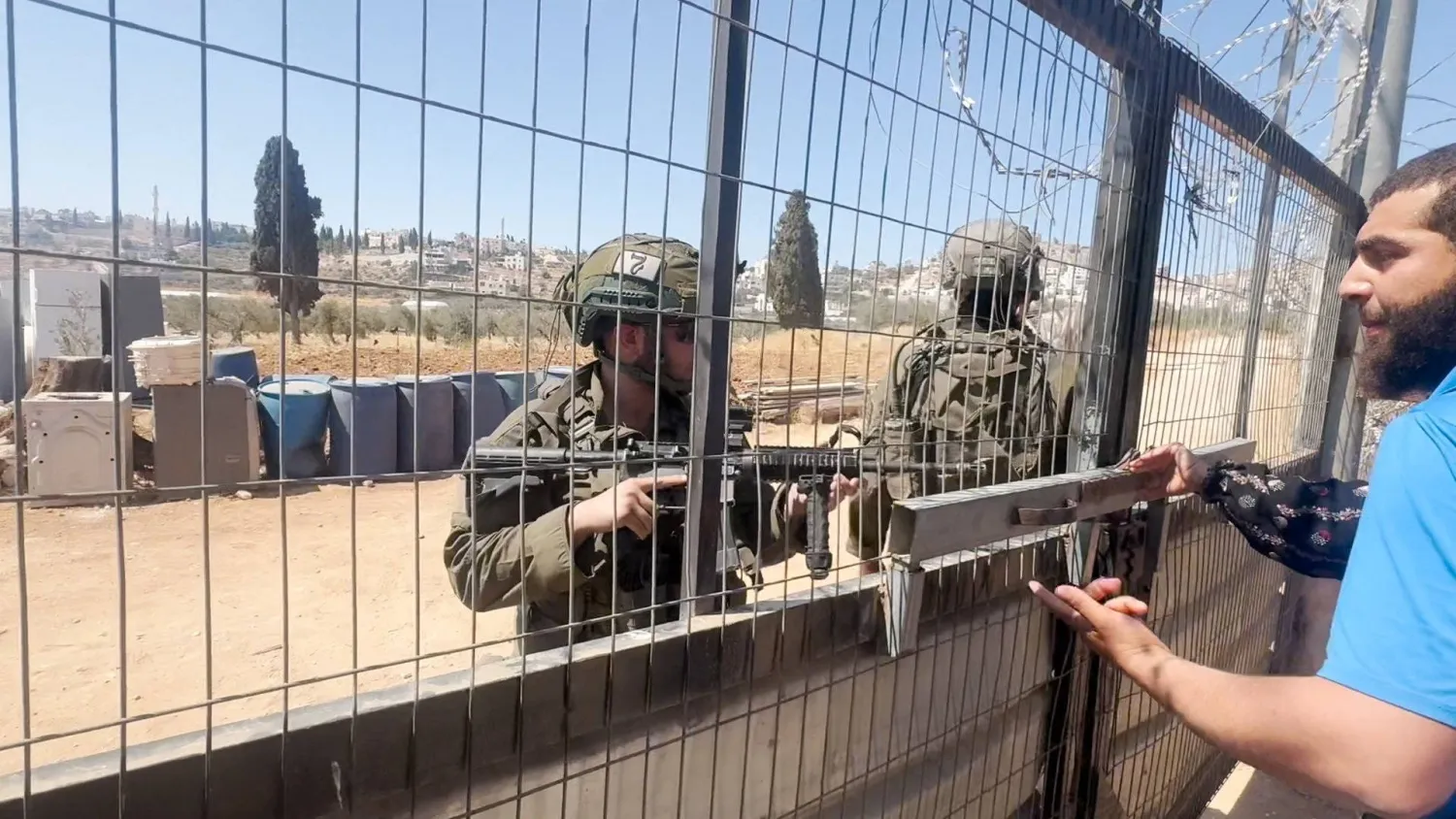 أحد عناصر القوات الإسرائيلية يتحدث إلى فلسطيني بينما يصوب سلاحاً باتجاهه في قرية المغير قرب رام الله (رويترز)