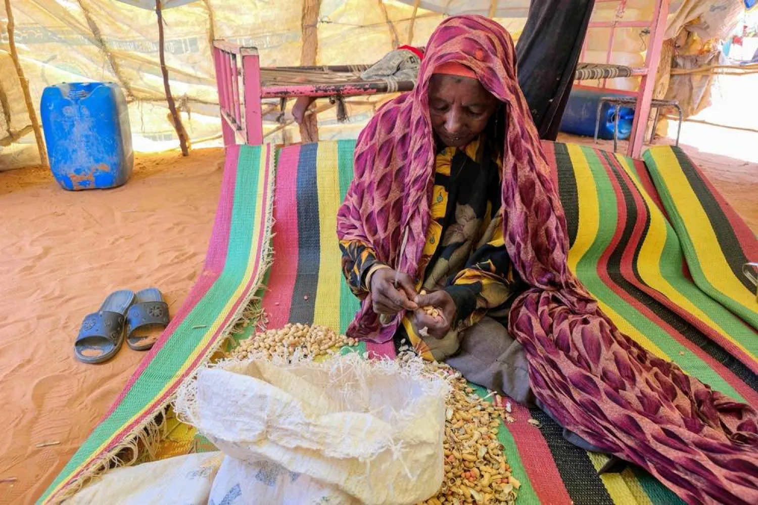 A Sudanese woman peels beans inside a shelter in the al-Rahmaniya camp for displaced people near the city of al-Obeid in the southern Kordofan region on July 9, 2026. (AFP)