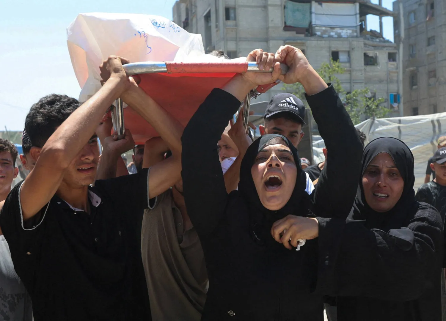 والدة الطفل الفلسطيني معتز أبو شعر الذي قُتل بنيران إسرائيلية ومشيعون يحملون جثمانه في خان يونس جنوب غزة يوم الثلاثاء (رويترز)