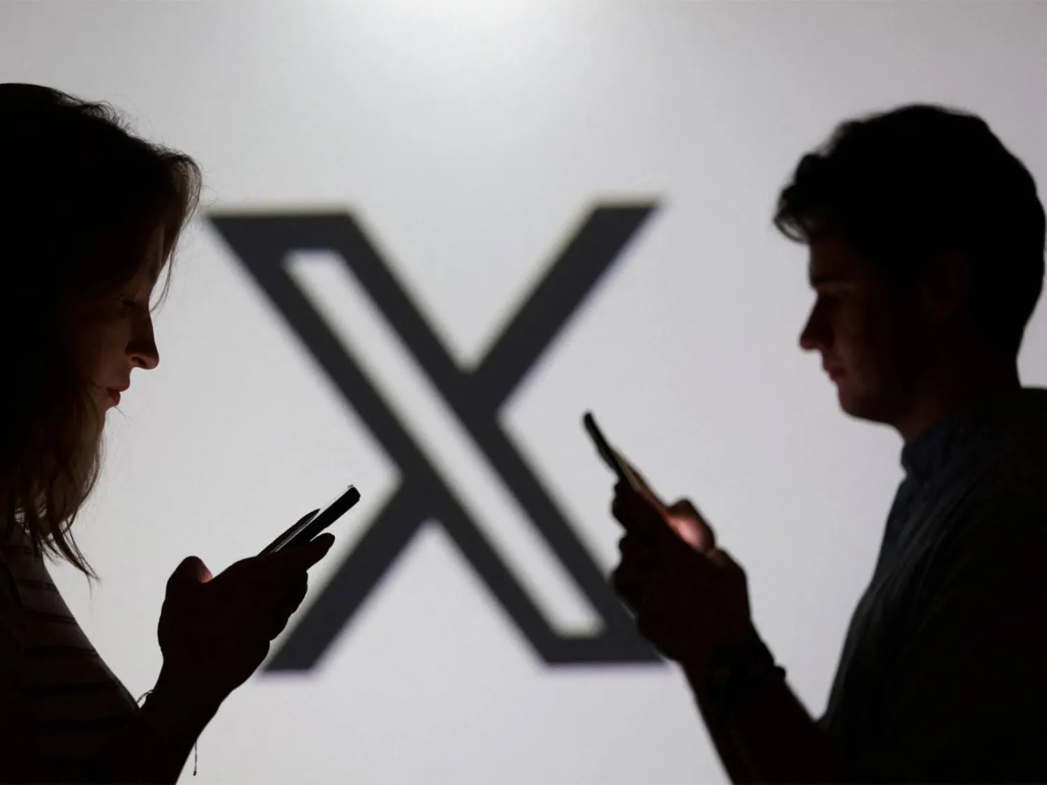 Teens pose for a photo while holding smartphones in front of the X logo. (Reuters) 