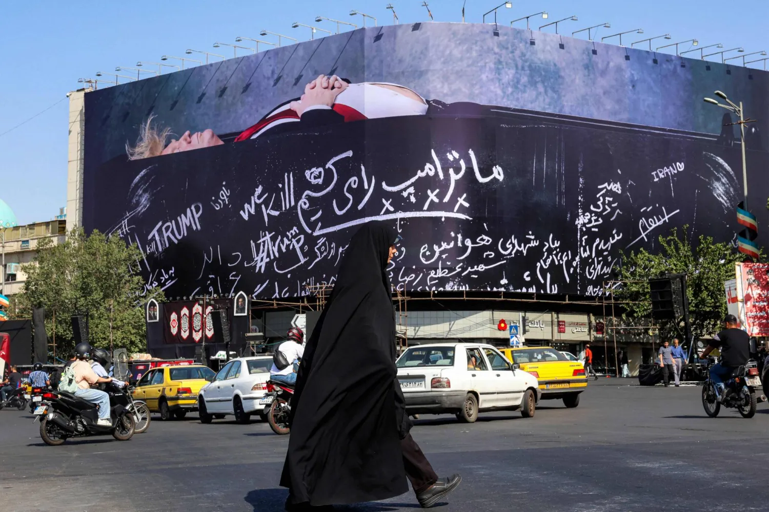 TOPSHOT - A woman crosses Tehran's Enghelab Square on July 15, 2026, past a giant anti-US billboard featuring US president Donald Trump in a coffin with text in Persian reading "We Kill Trump".  (Photo by AFP)  