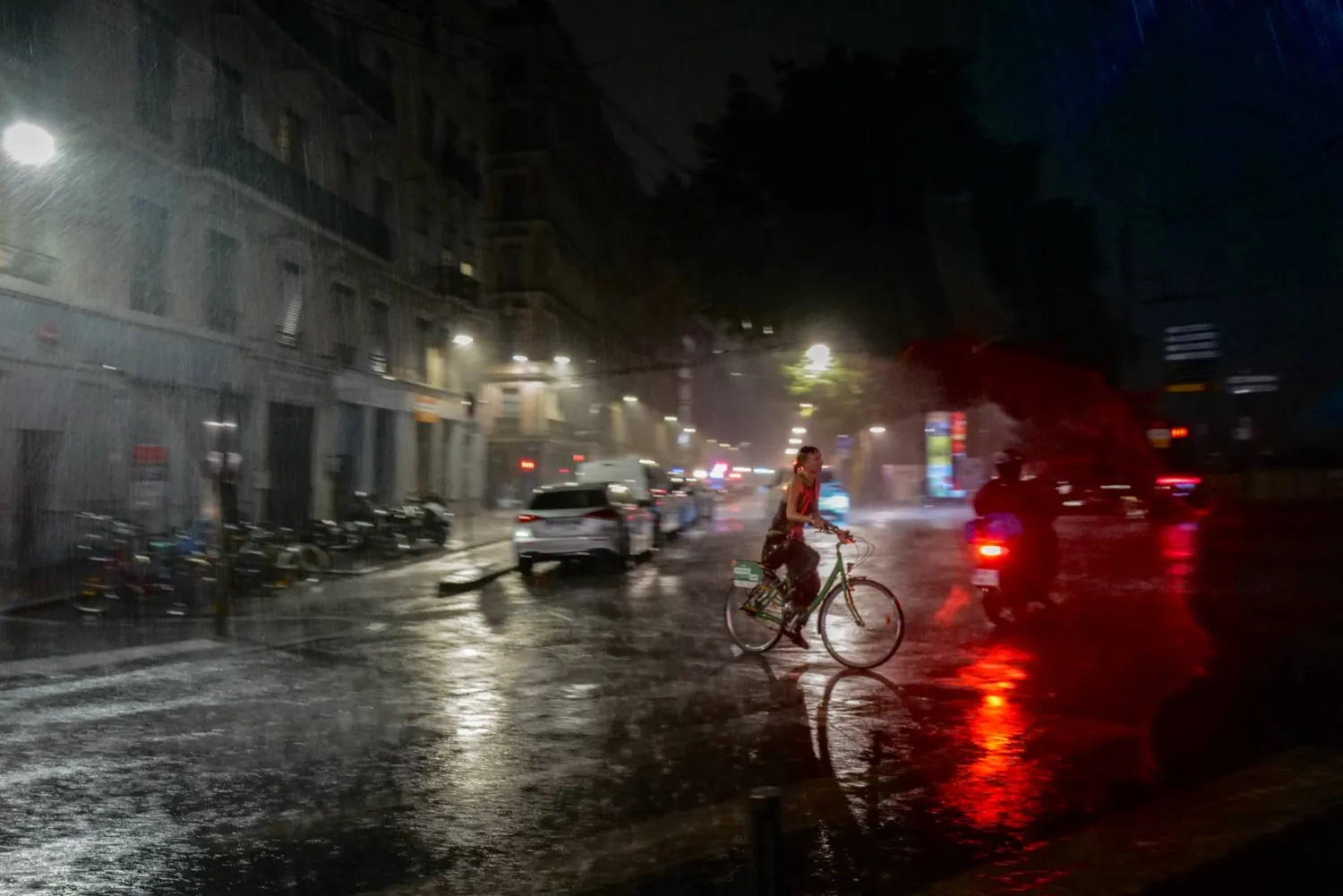 A woman rides a bicycle during a rainstorm in central Lyon on 16 July, 2026. (Photo by OLIVIER CHASSIGNOLE / AFP)