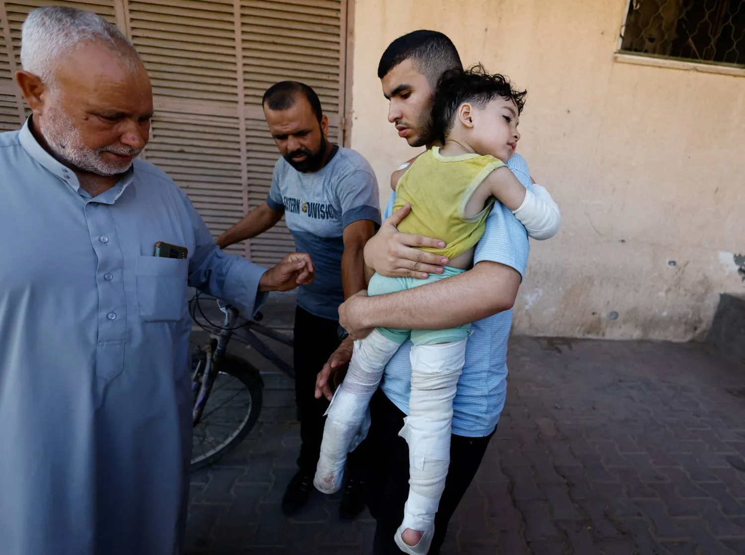 فلسطيني يحمل طفلاً أصيب بغارة إسرائيلية قتلت والديه في مستشفى «شهداء الأقصى» بدير البلح وسط قطاع غزة الأربعاء (رويترز)