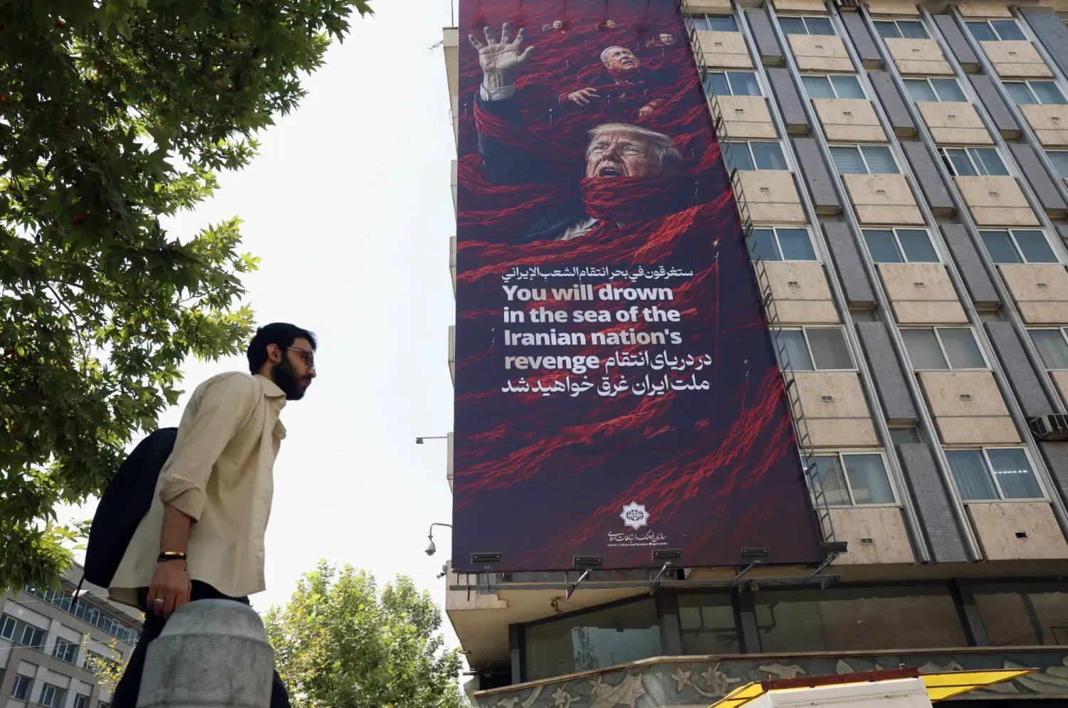 Tahran’da bir binaya asılan devasa propaganda afişinde, ABD Başkanı Donald Trump ile İsrail Başbakanı Binyamin Netanyahu’nun resimleri yer alıyor ve afişin üzerinde “İran halkının intikam denizinde boğulacaksın” yazıyor. (EPA)