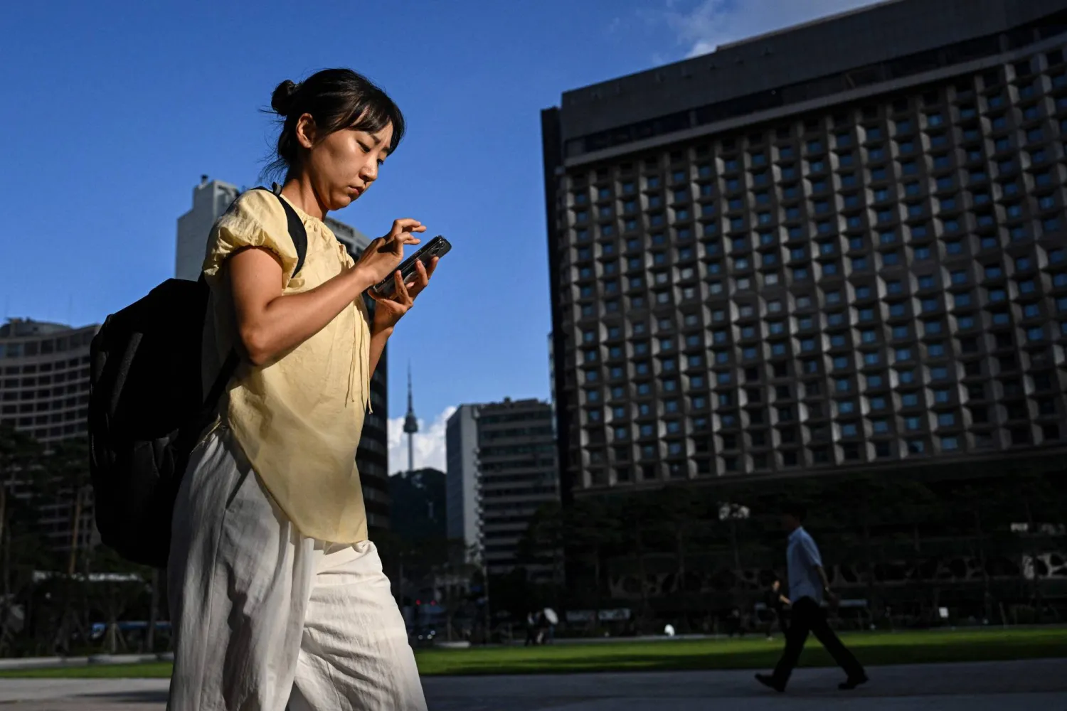 A woman checks her phone as she walks along a street in Seoul on July 13, 2026. (AFP)