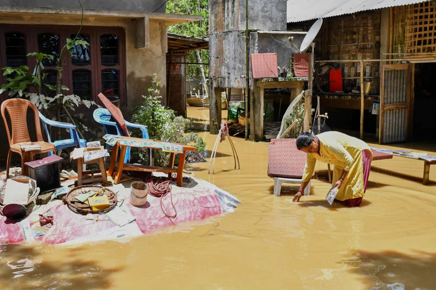A woman salvages belongings outside her house damaged by floodwaters following heavy rains in Assam's Jorhat district on July 21, 2026. (AFP)